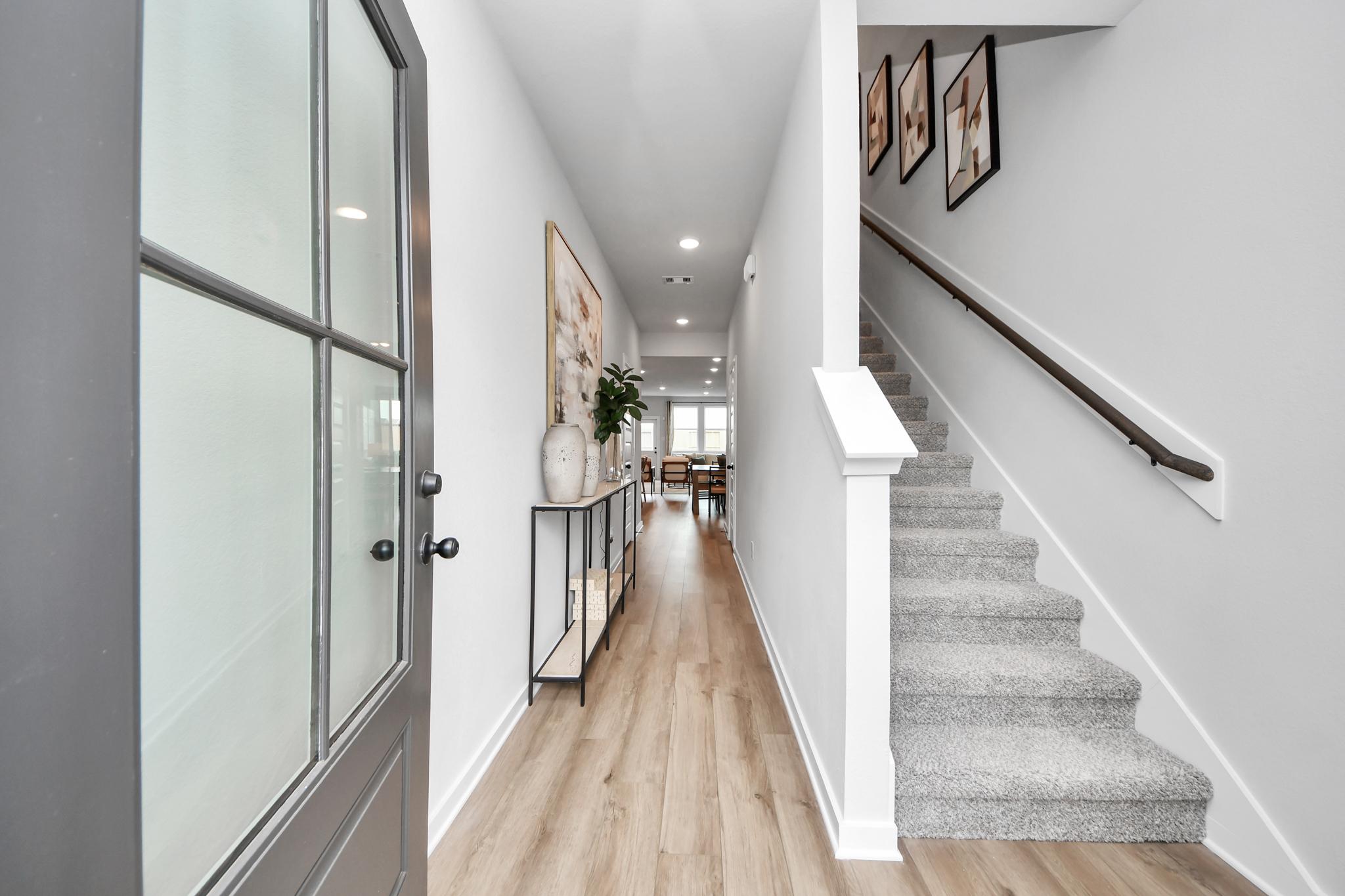 Bright entryway at Robins Landing in Houston, TX by Davidson Homes with wood flooring and carpeted staircase.