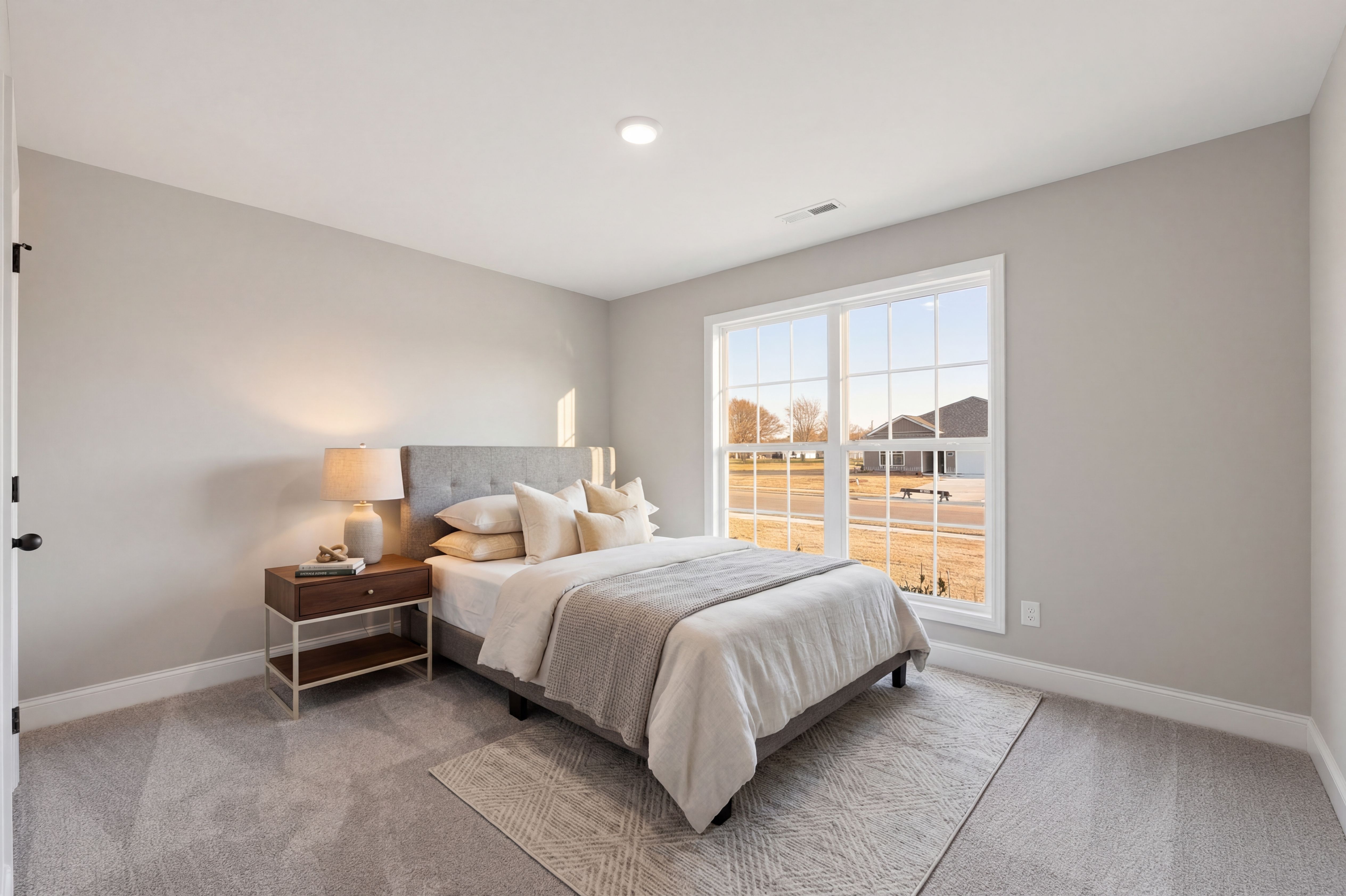 Spacious gray bedroom at Chapel Hill in Athens Alabama with upholstered bed, nightstand lamp, and large window overlooking neighborhood
