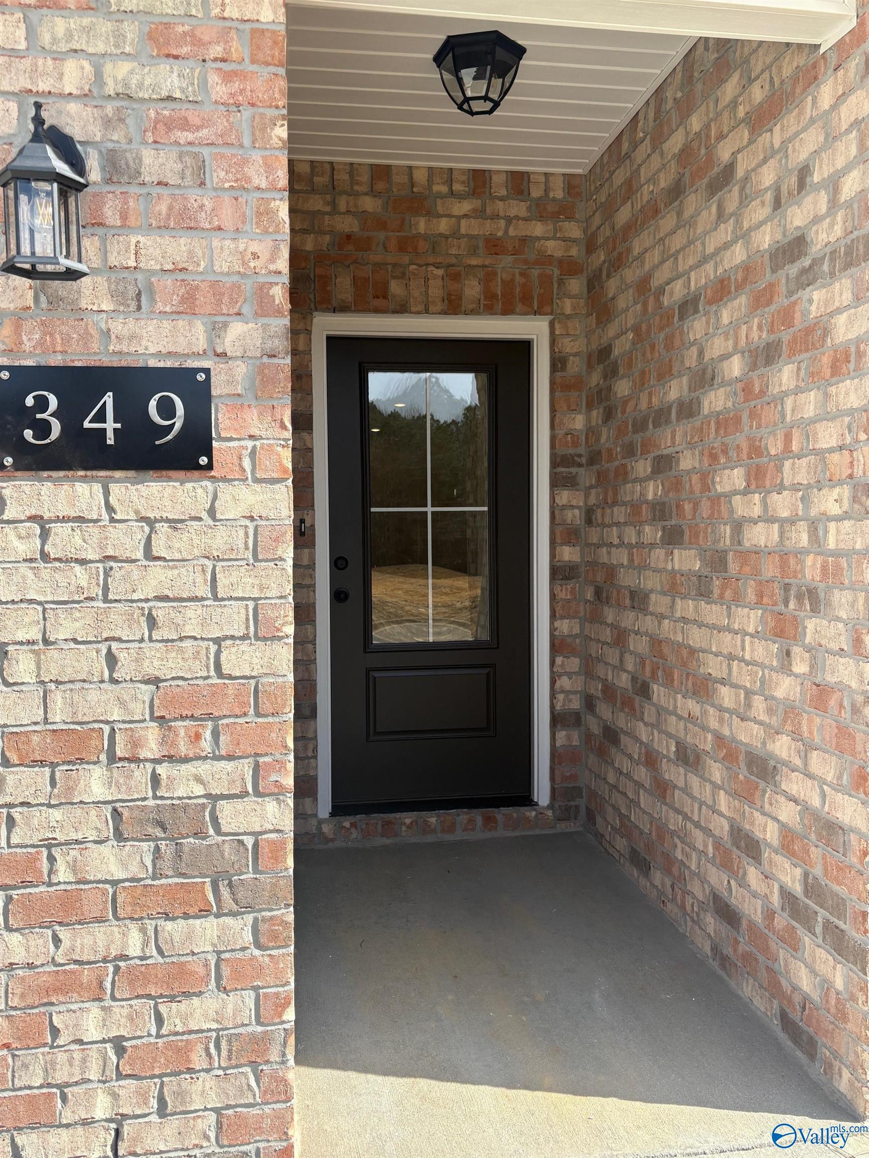 Brick front entrance featuring black glass-paneled door, house number 349, and lantern lighting in Davidson Homes The Asheville C, Arab, Alabama