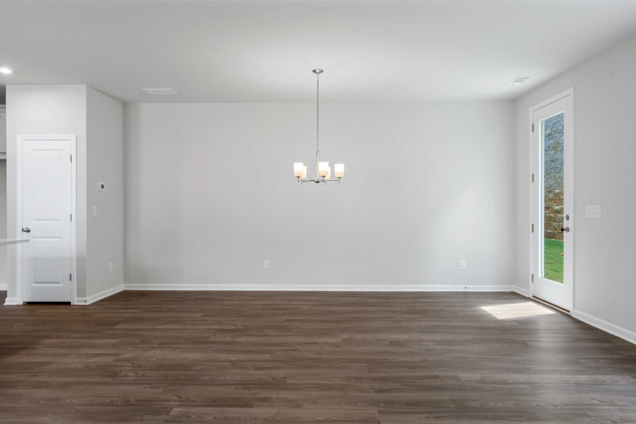 Spacious empty dining area in The Cary A home with hardwood floors, modern chandelier, and glass French doors