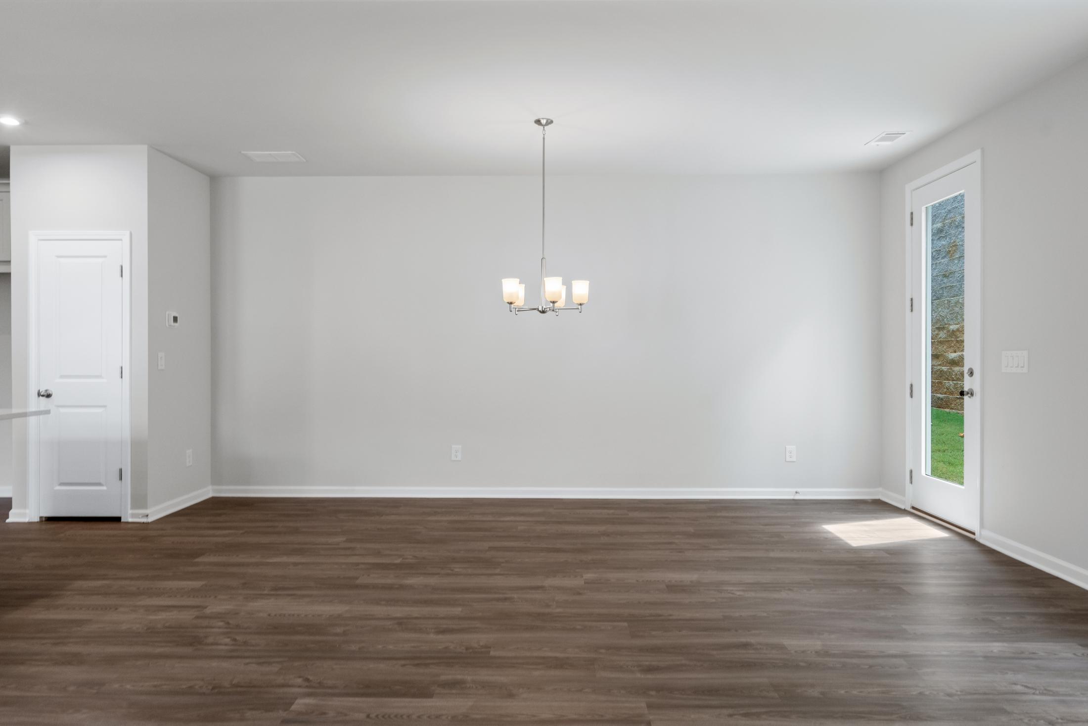 Spacious empty dining area in The Cary A home with hardwood floors, modern chandelier, and glass French doors