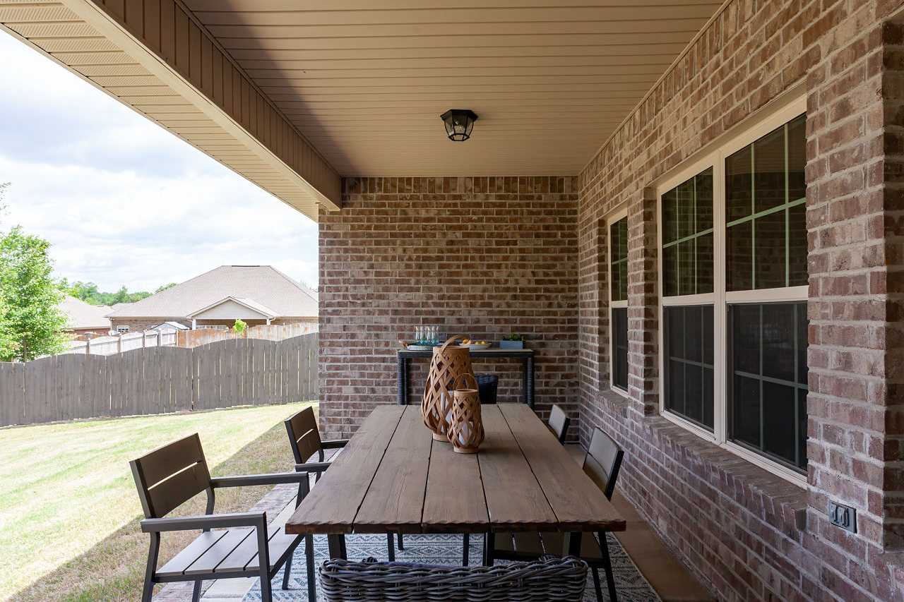 Spacious covered brick patio at Laurenwood Preserve in Madison Alabama featuring wooden dining table, wicker chairs, and woven rug