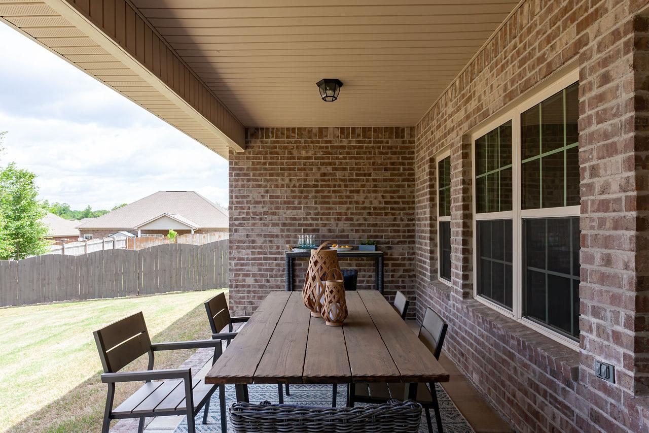 Spacious covered brick patio at Laurenwood Preserve in Madison Alabama featuring wooden dining table, wicker chairs, and woven rug