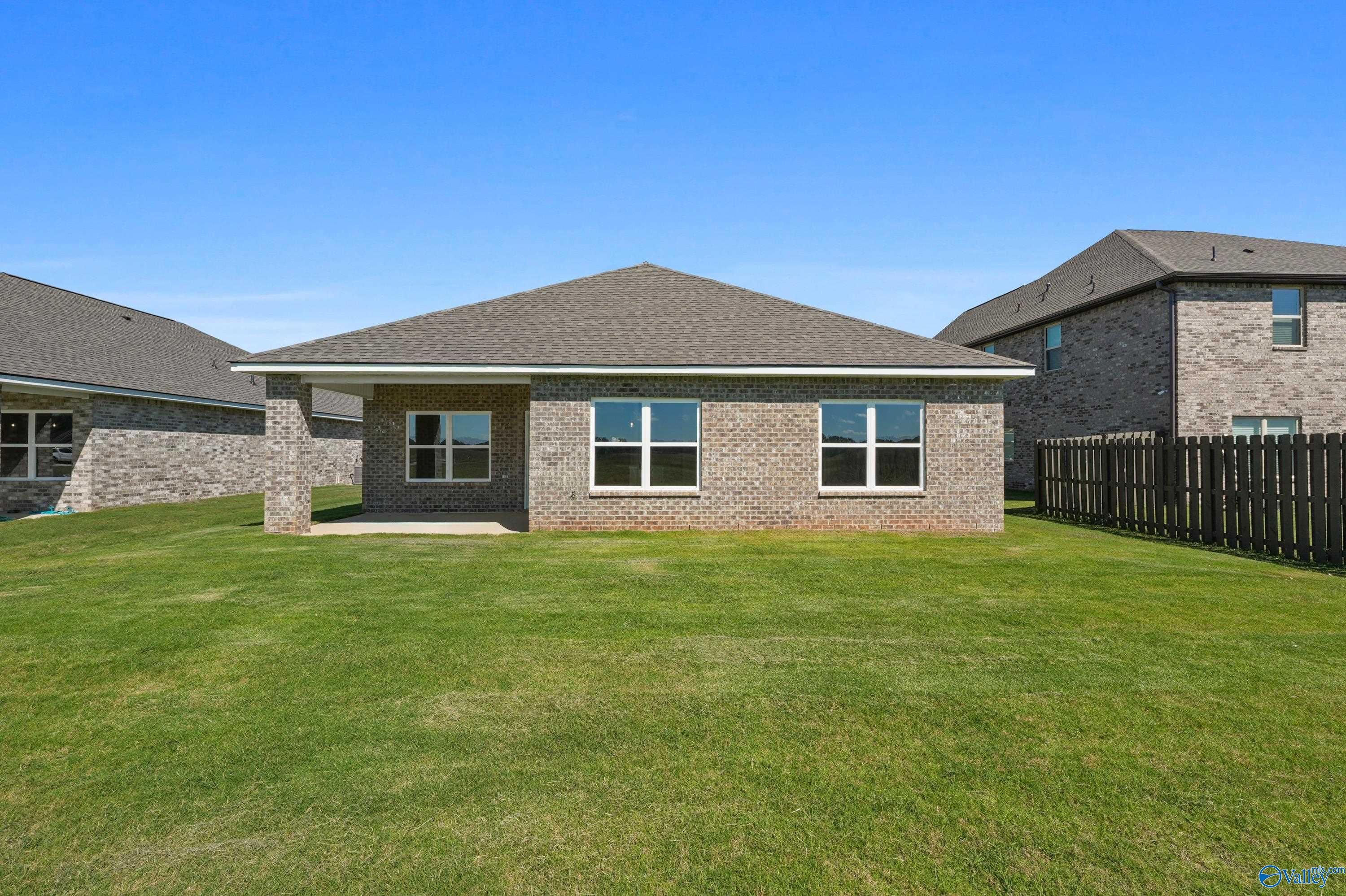 Single-story brick ranch home with gabled roof, covered porch, double windows, lush green yard, and privacy fence in Clearview, Hazel Green, Alabama