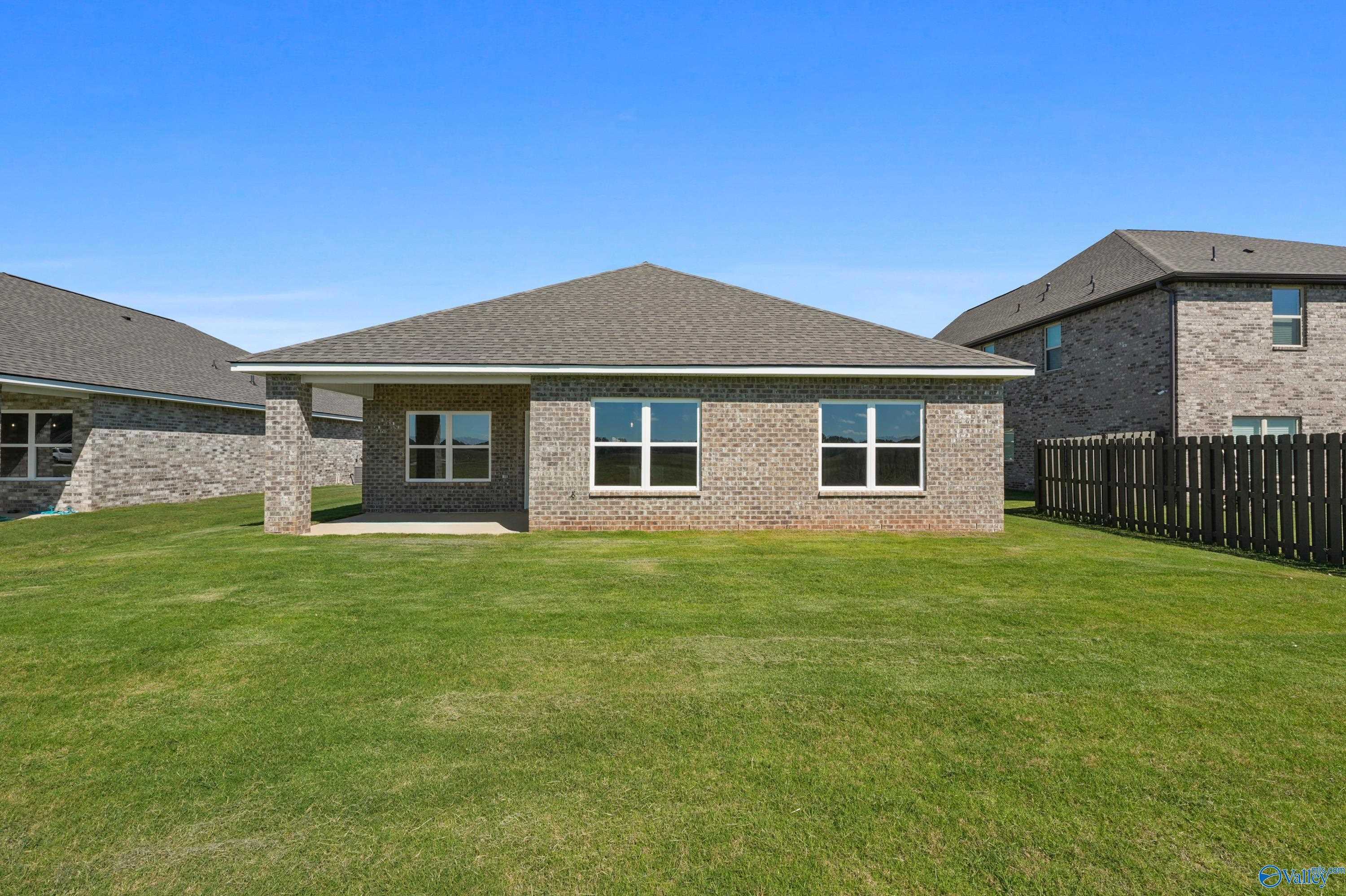 Single-story brick ranch home with gabled roof, covered porch, double windows, lush green yard, and privacy fence in Clearview, Hazel Green, Alabama
