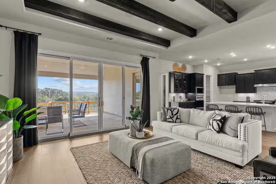 Bright living room with beamed ceiling, white sofa, sliding doors to covered patio and hill views in Davidson Homes Summerlin B, Castroville Texas