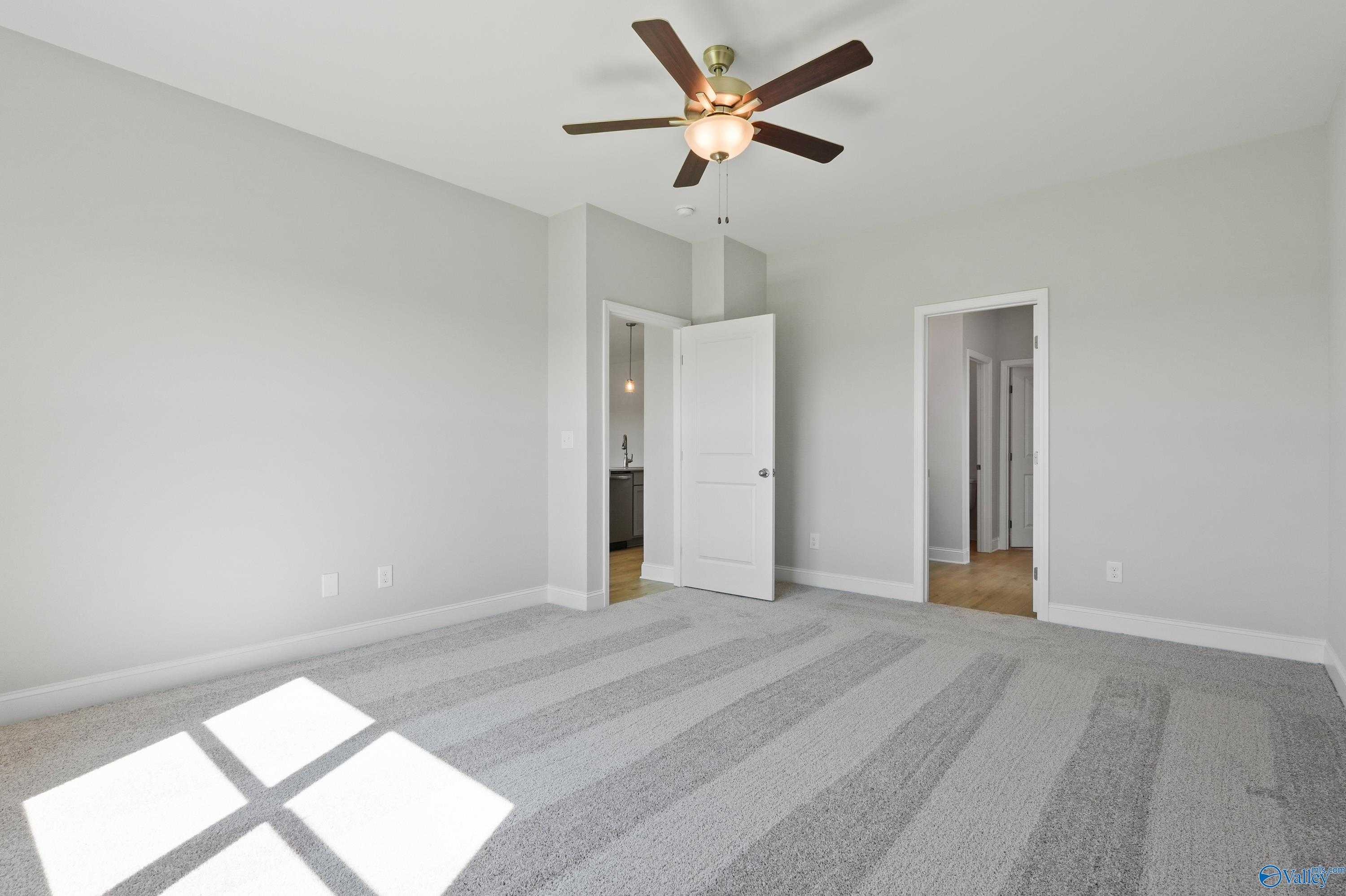 Bright bedroom with gray carpet, ceiling fan, and adjacent bath in Davidson Homes The Everett, Hazel Green, AL