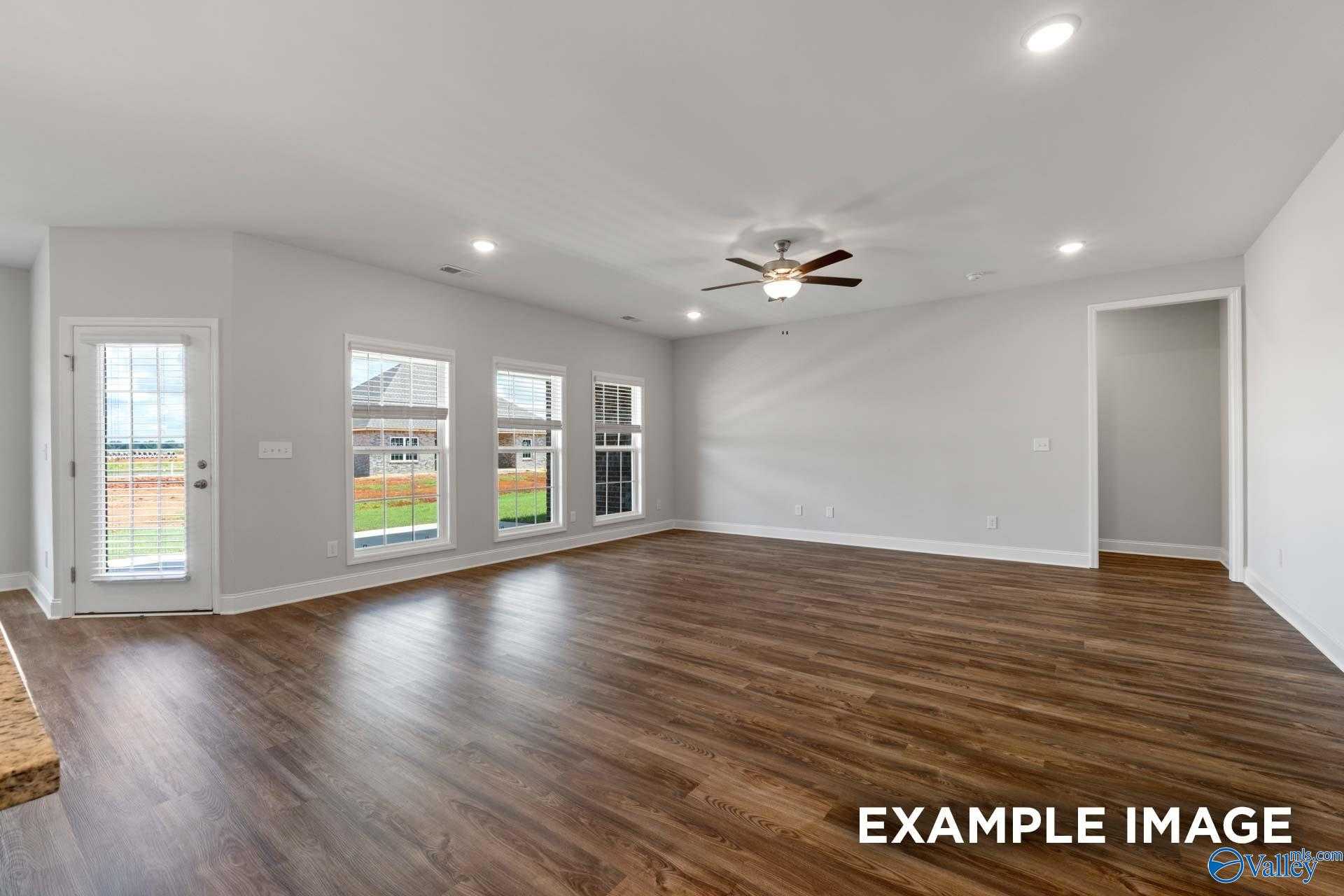 Bright open-concept living room with hardwood floors, ceiling fan, and large windows overlooking lawn in The Harrison B, Decatur, AL