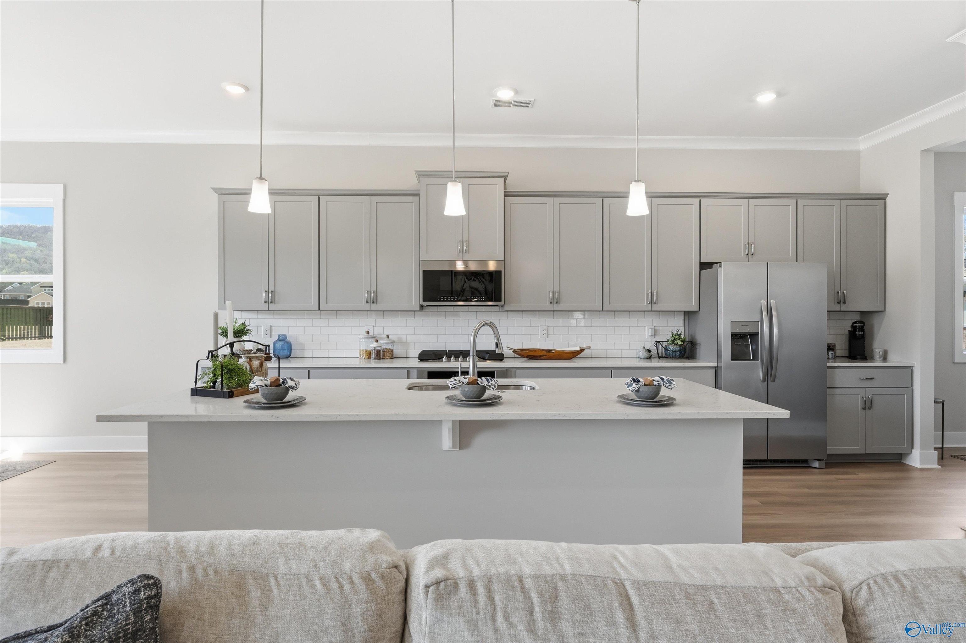 Modern gray kitchen with quartz island, stainless steel appliances, subway tile backsplash in Evermore Homes The Oxford B, Owens Cross Roads, AL