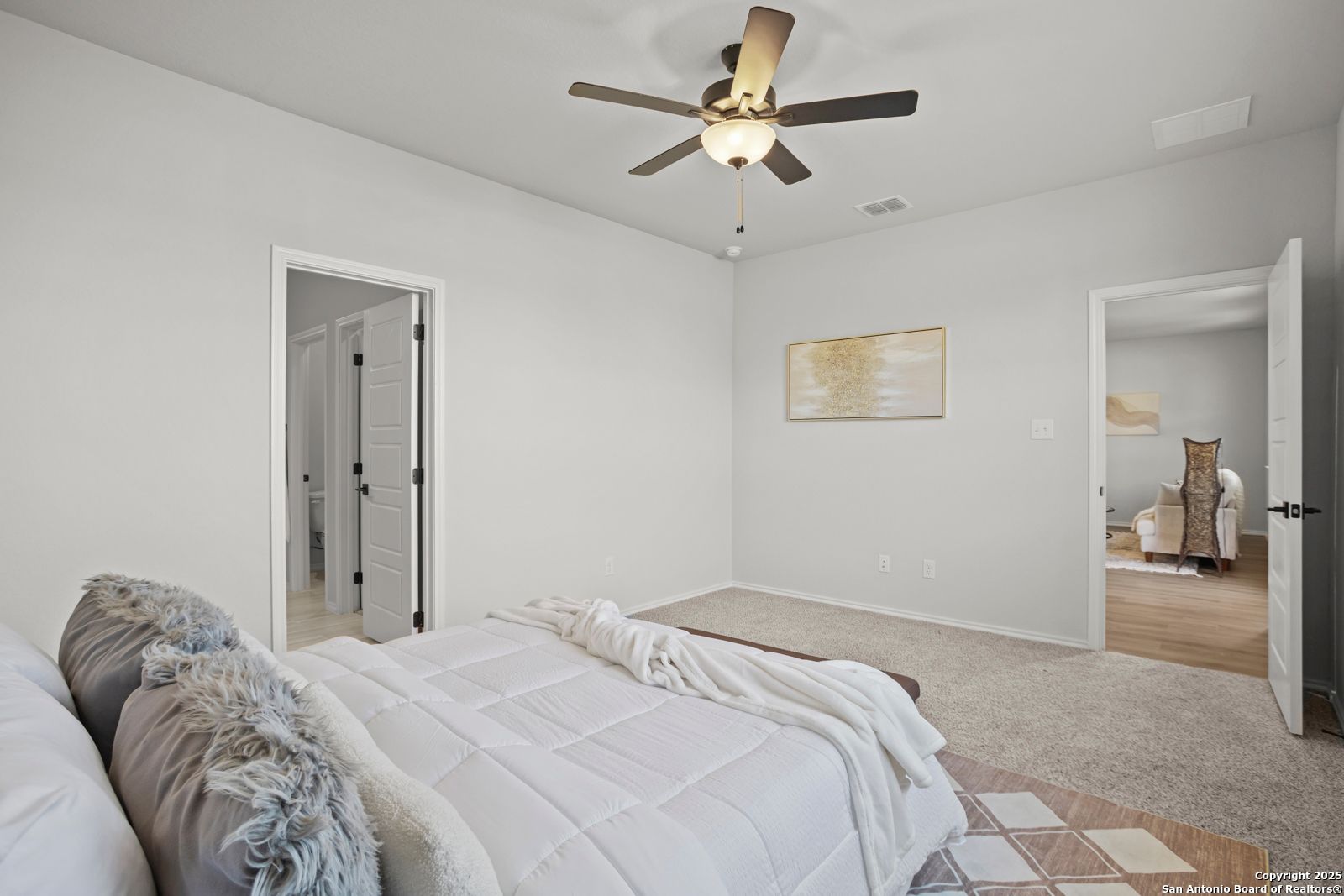 Cozy bedroom with ceiling fan, plush white bed, gray pillows, and abstract art in Davidson Homes The Douglas C, Seguin, Texas