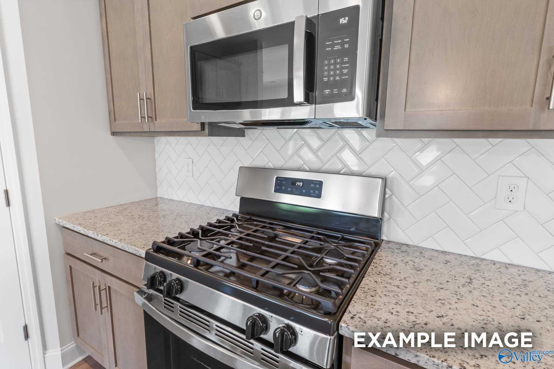 Modern kitchen featuring stainless steel gas range, microwave, subway tile backsplash, and granite counters in Davidson Homes The Daphne D, Arab, Alabama