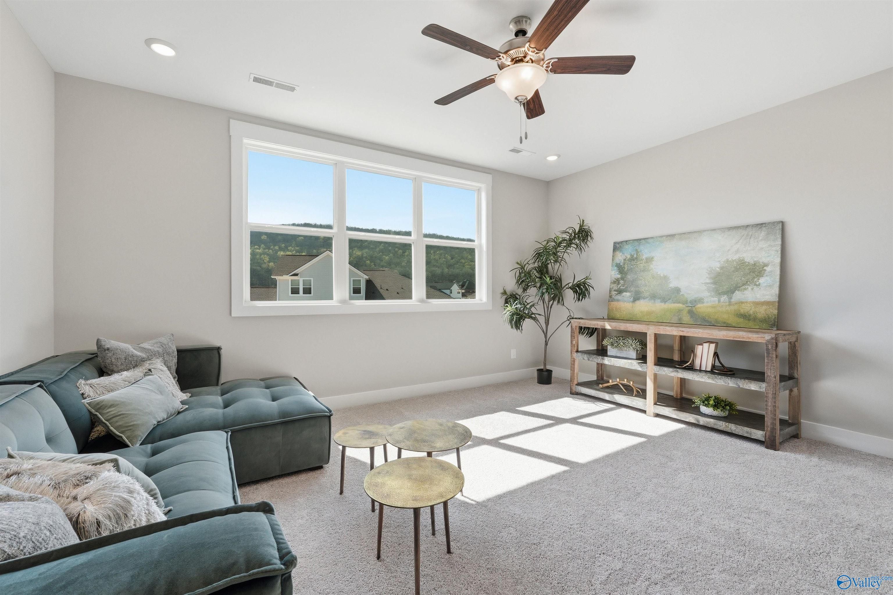 Cozy bonus room featuring teal velvet sectional, wooden console with landscape art, brass tables, and hill views in Evermore Homes The Oxford B, Owens Cross Roads, Alabama