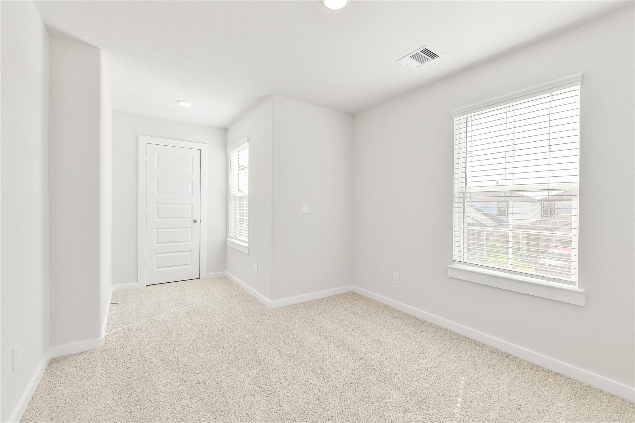 Bright secondary bedroom with neutral carpet, white walls, window blinds, and door in Davidson Homes The Blanco E, Magnolia, Texas
