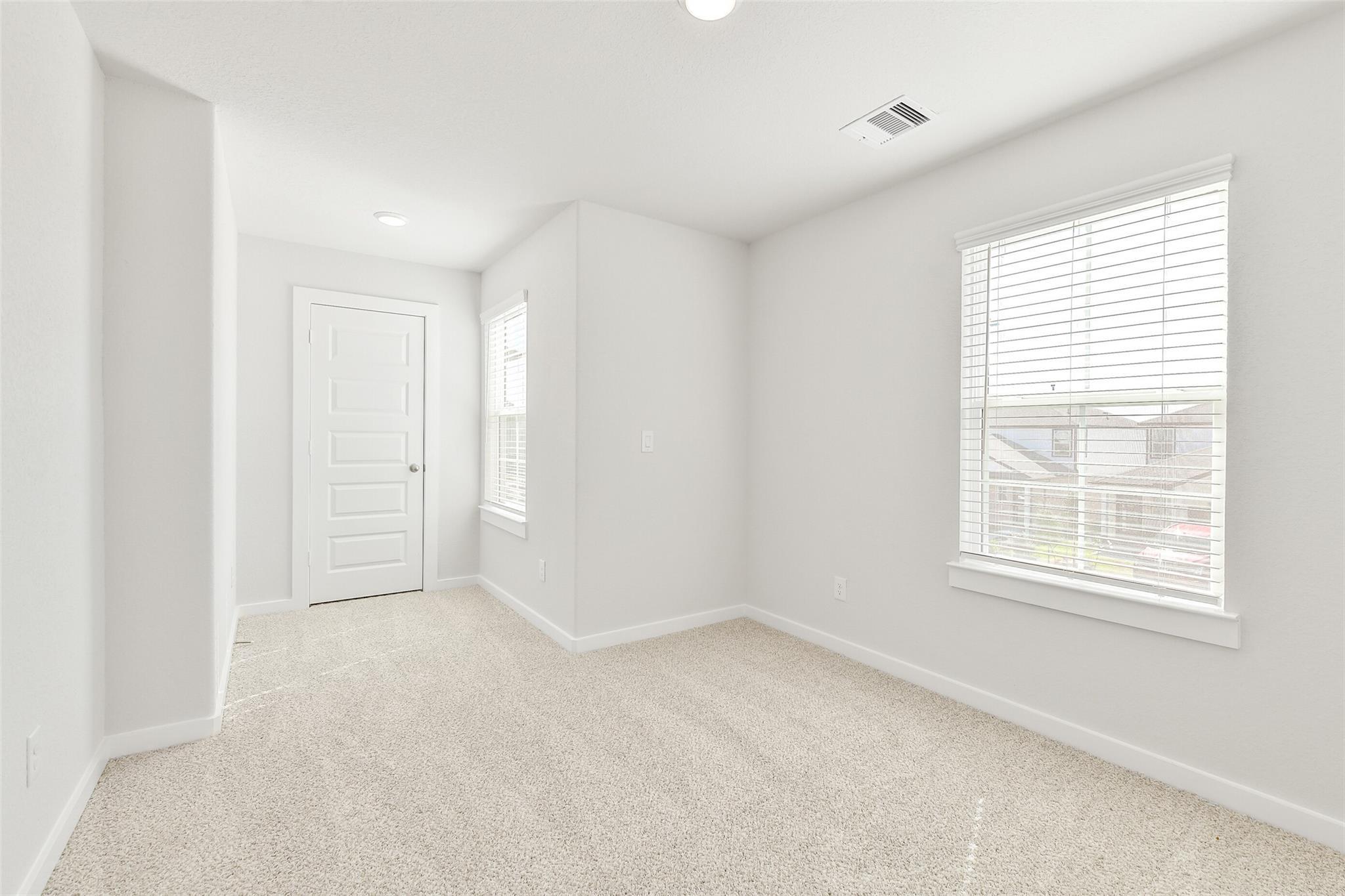 Bright secondary bedroom with neutral carpet, white walls, window blinds, and door in Davidson Homes The Blanco E, Magnolia, Texas