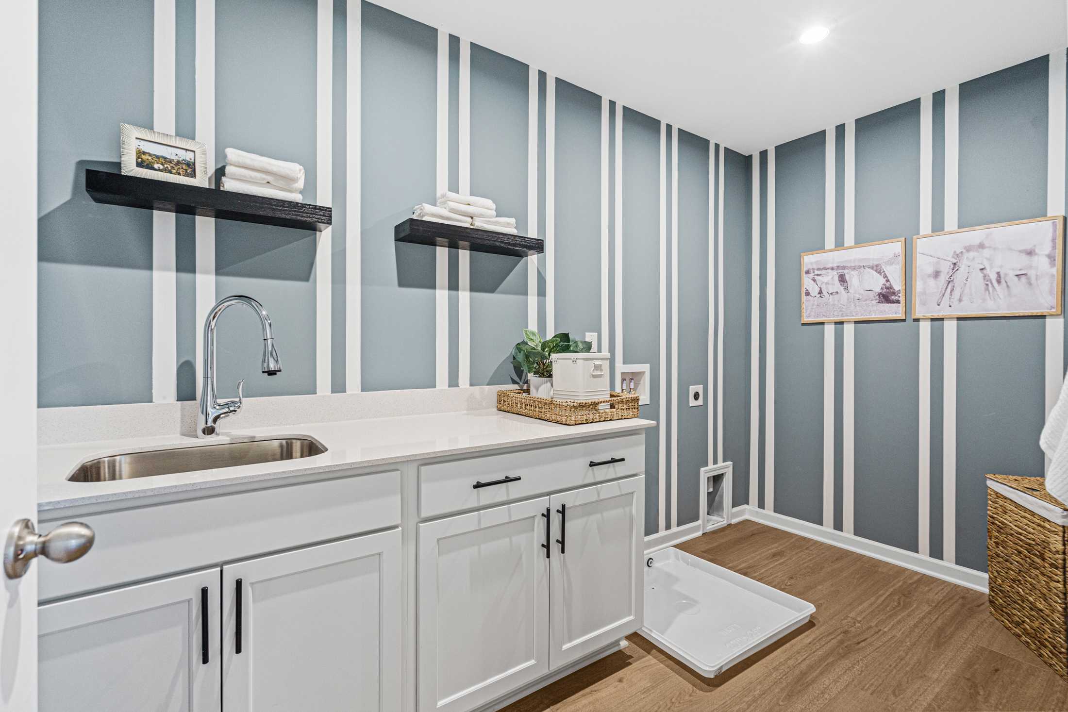 Spacious laundry room in The Hickory A with blue striped walls, white shaker cabinets, utility sink, shelves, and pet door