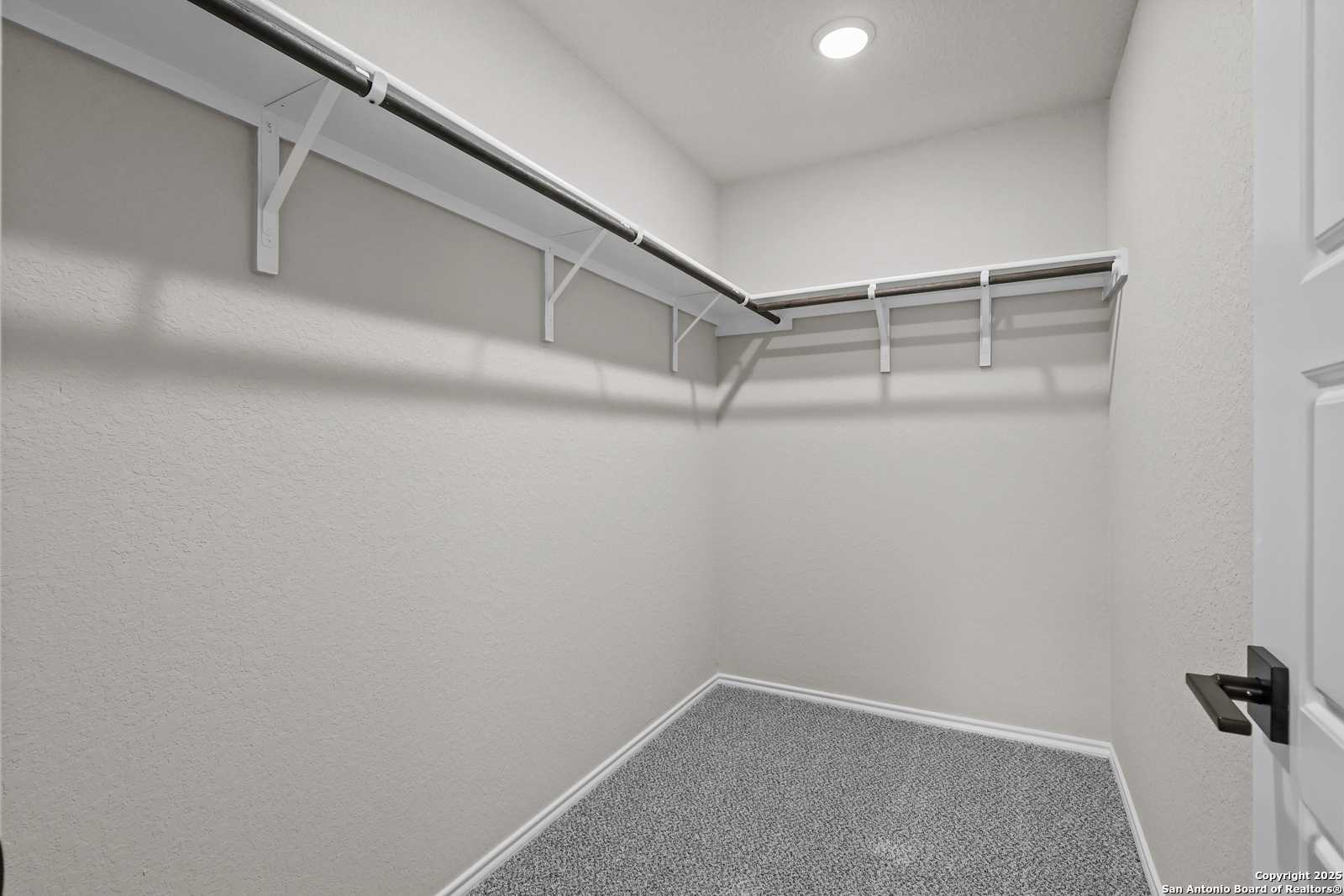 Spacious walk-in closet with white shelving, beige walls, and gray carpet in Davidson Homes The Charlotte B, San Antonio, Texas