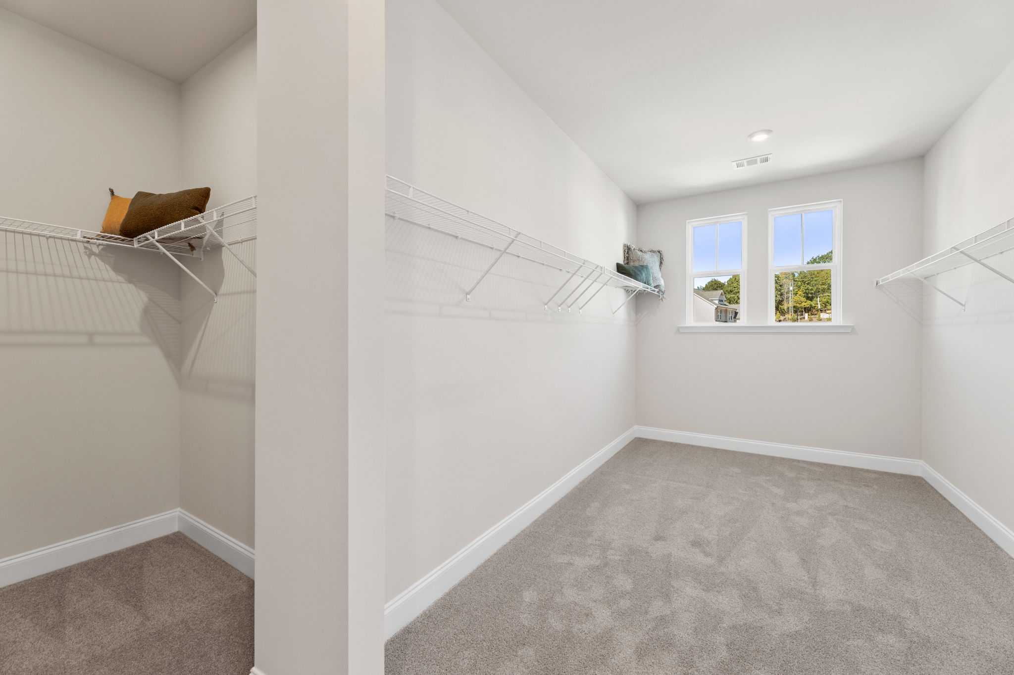 Spacious walk-in closet with wire shelving, neutral walls, gray carpet, and window view at Melody Lakeside Estates in Buford GA by Davidson Homes
