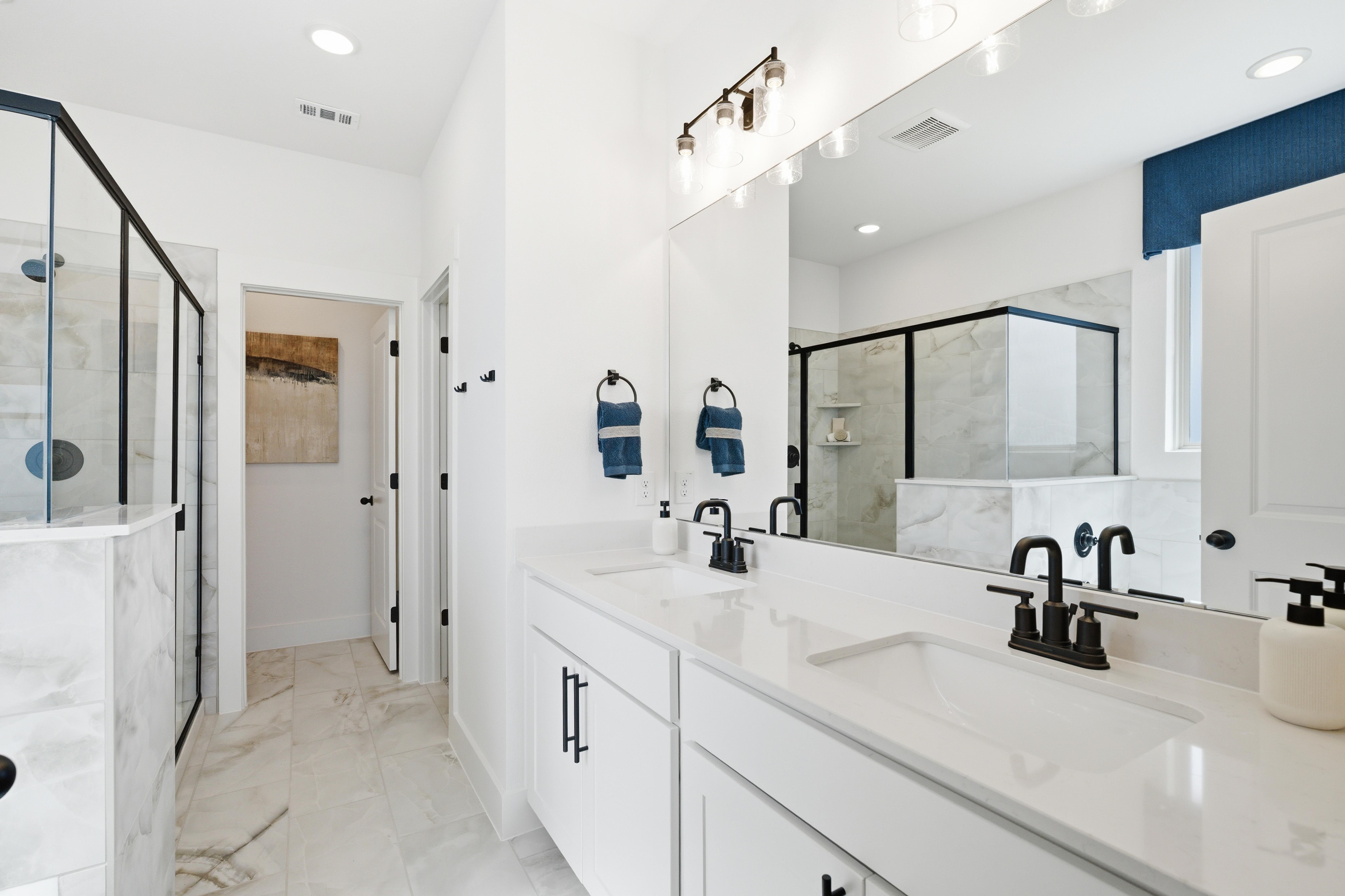 Modern master bathroom at Mercer Meadows in Royse City TX with white double vanity, blue accents, and glass shower