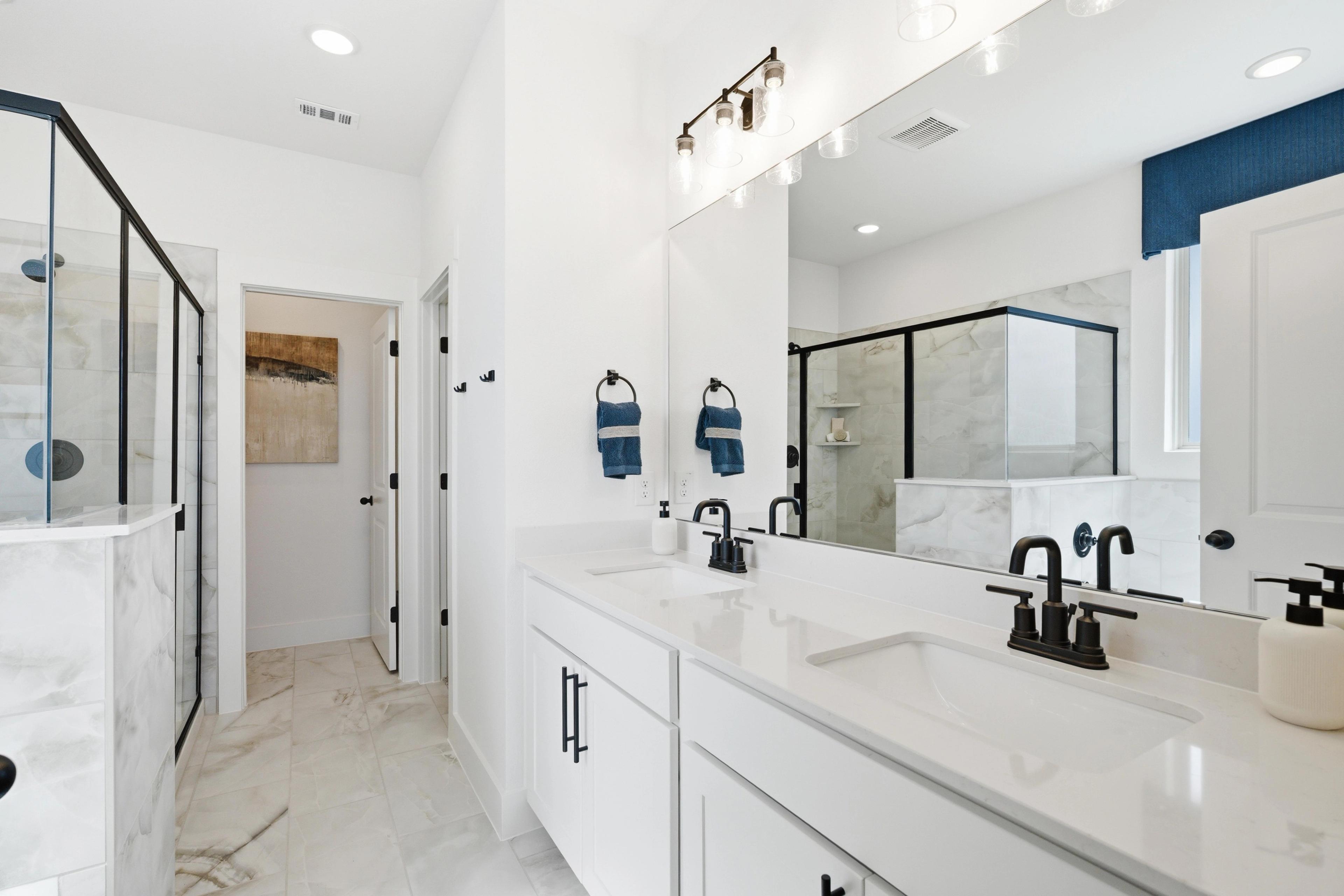 Modern master bathroom at Mercer Meadows in Royse City TX with white double vanity, blue accents, and glass shower