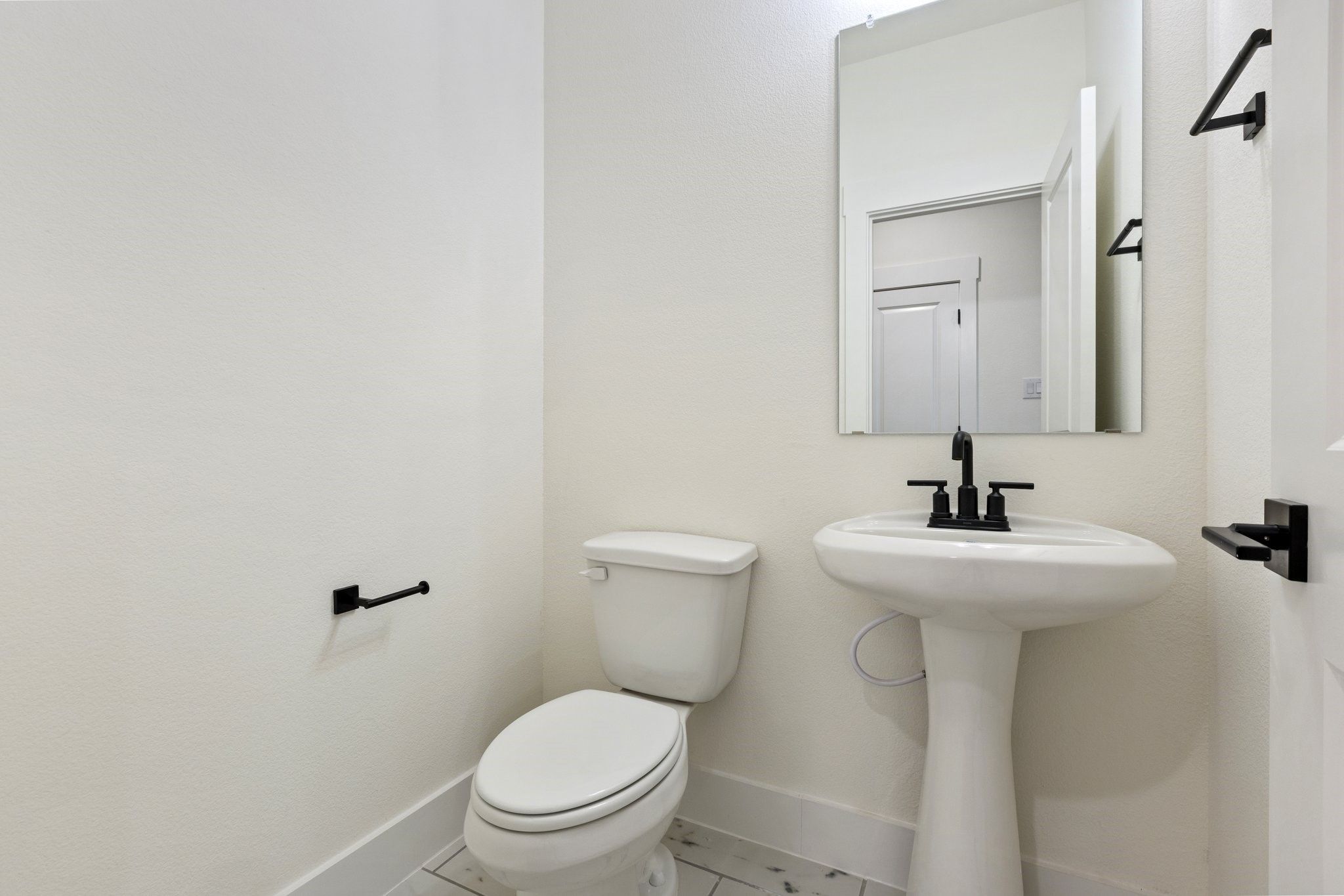 Modern powder room with pedestal sink, matte black fixtures, and mirror in The Rockford C floor plan, Waverly Estates.
