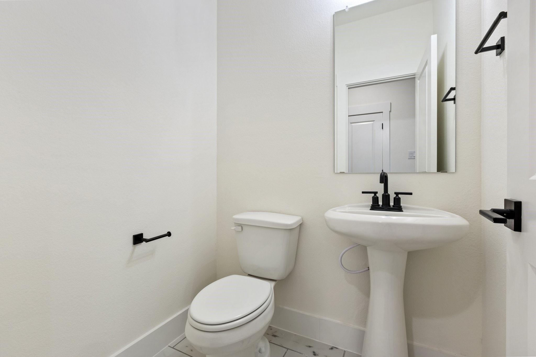 Modern powder room with pedestal sink, matte black fixtures, and mirror in The Rockford C floor plan, Waverly Estates.