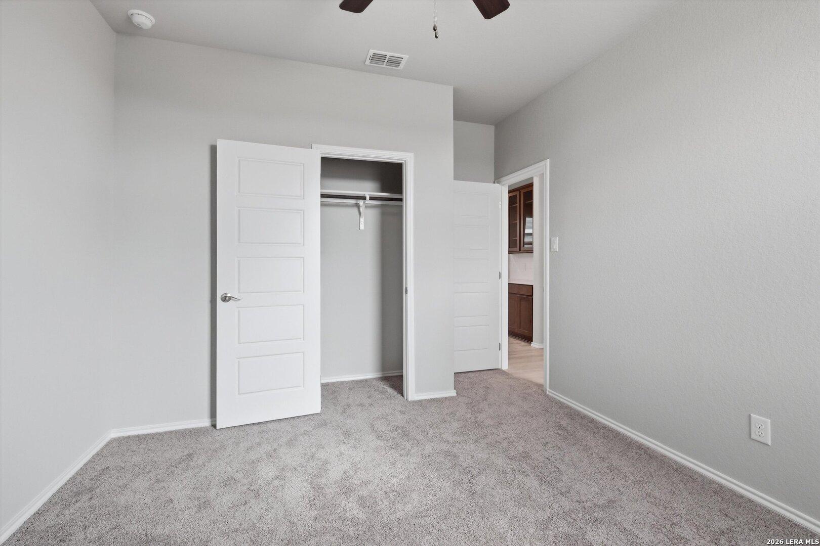 Spacious bedroom with open walk-in closet, ceiling fan, and bath door in Davidson Homes The Frio B, Agave San Antonio Texas