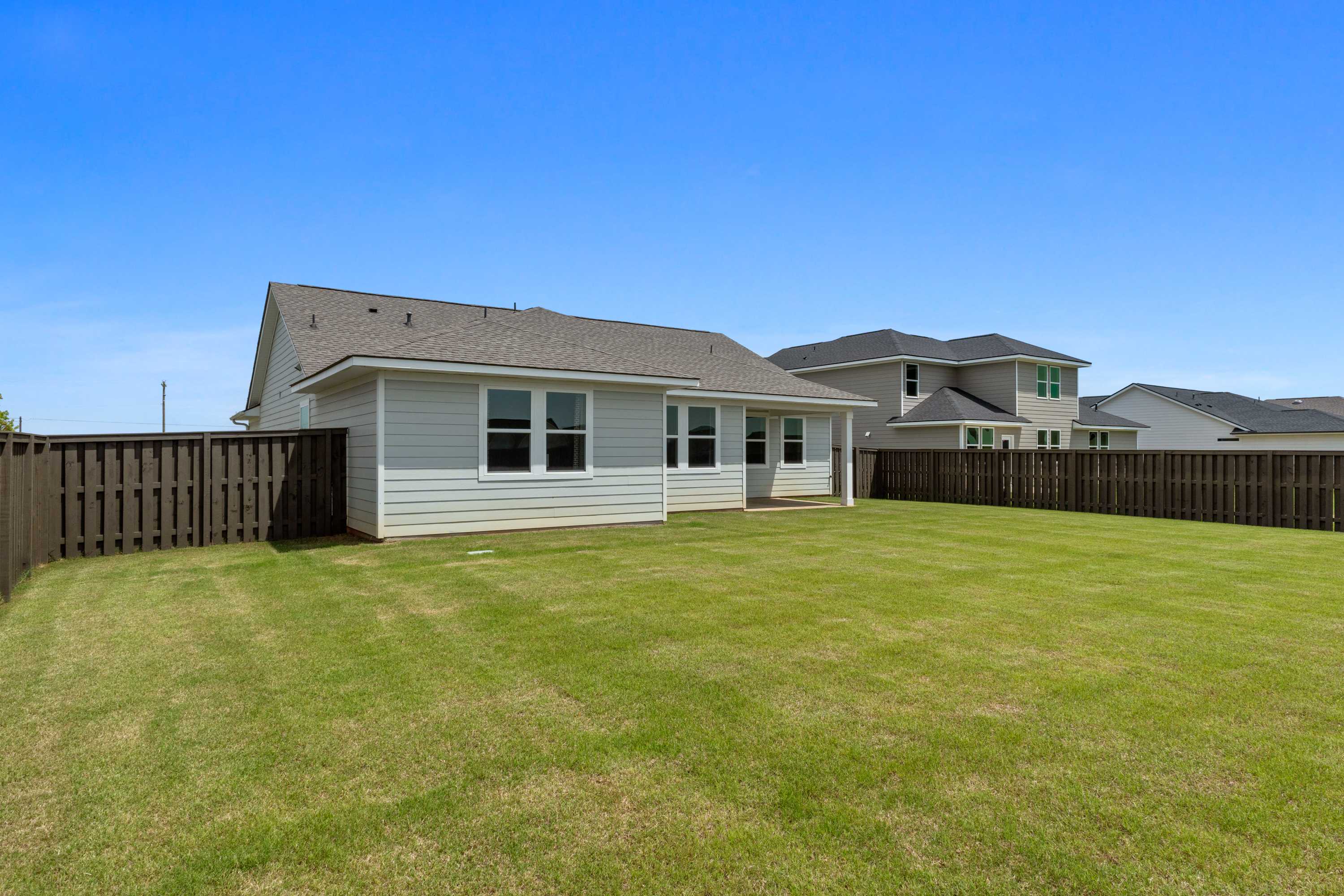 Spacious fenced backyard at Anderson Farm in Athens Alabama with white-sided home, lush green lawn, and blue sky