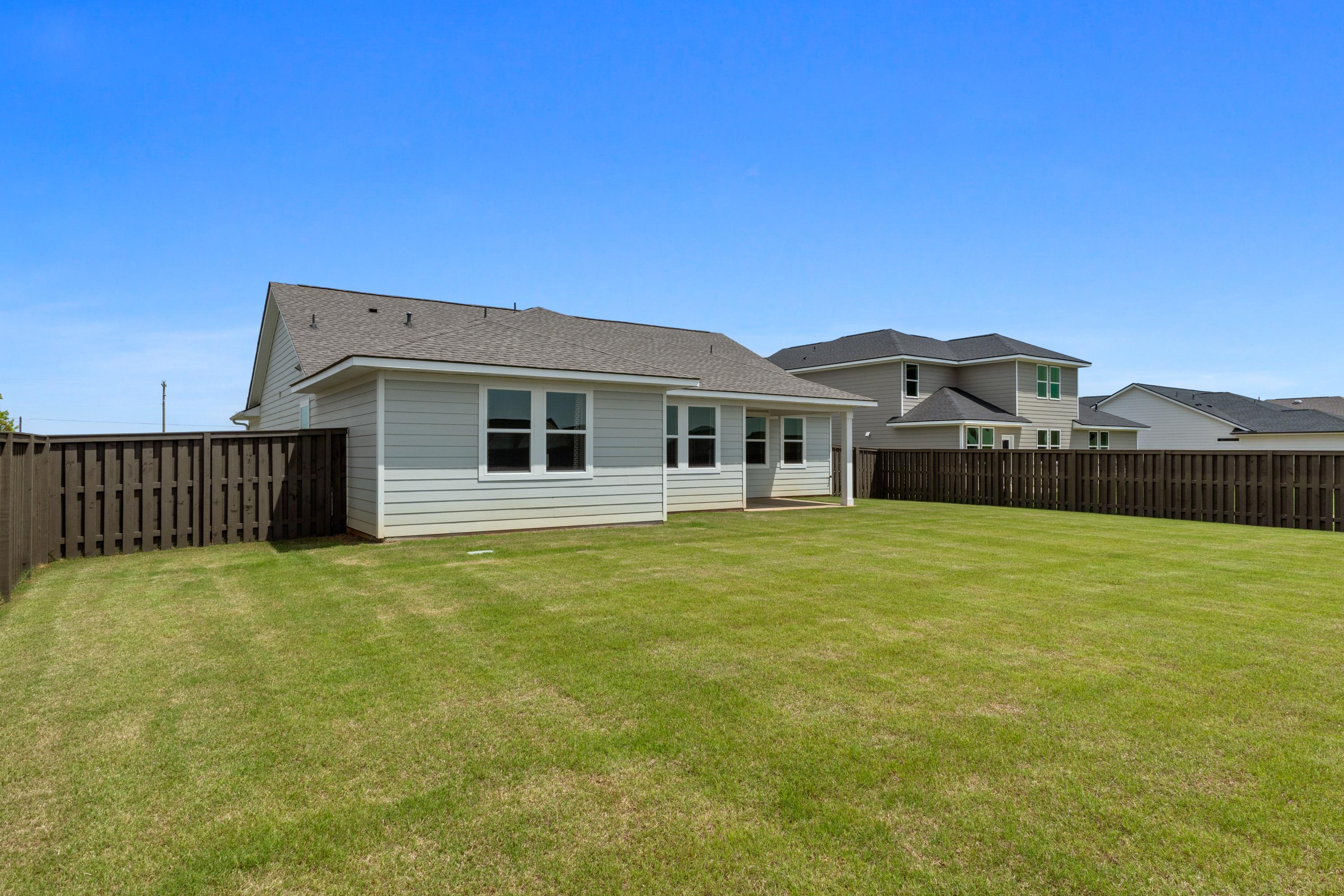 Spacious fenced backyard at Anderson Farm in Athens Alabama with white-sided home, lush green lawn, and blue sky