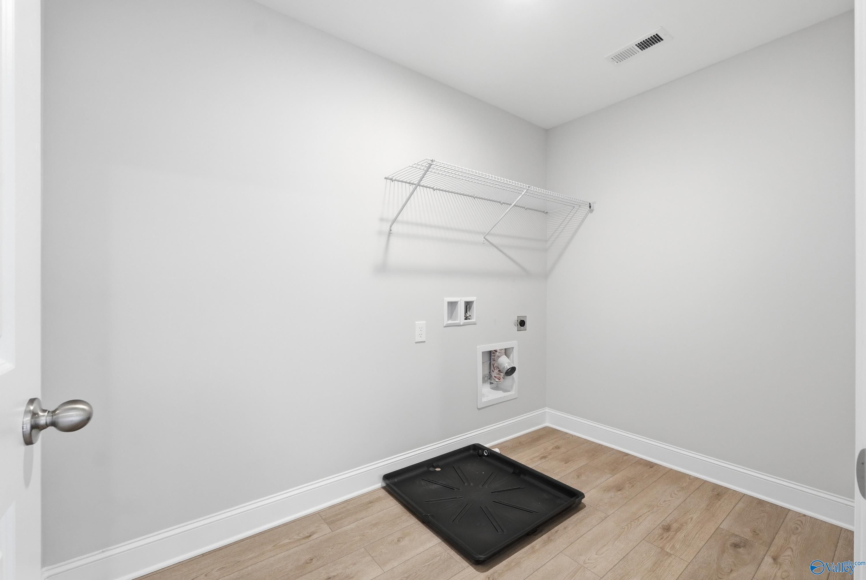 Modern laundry room with washer/dryer hookups, hanging rod, and hardwood floors in Davidson Homes The Shelby B, New Market, Alabama