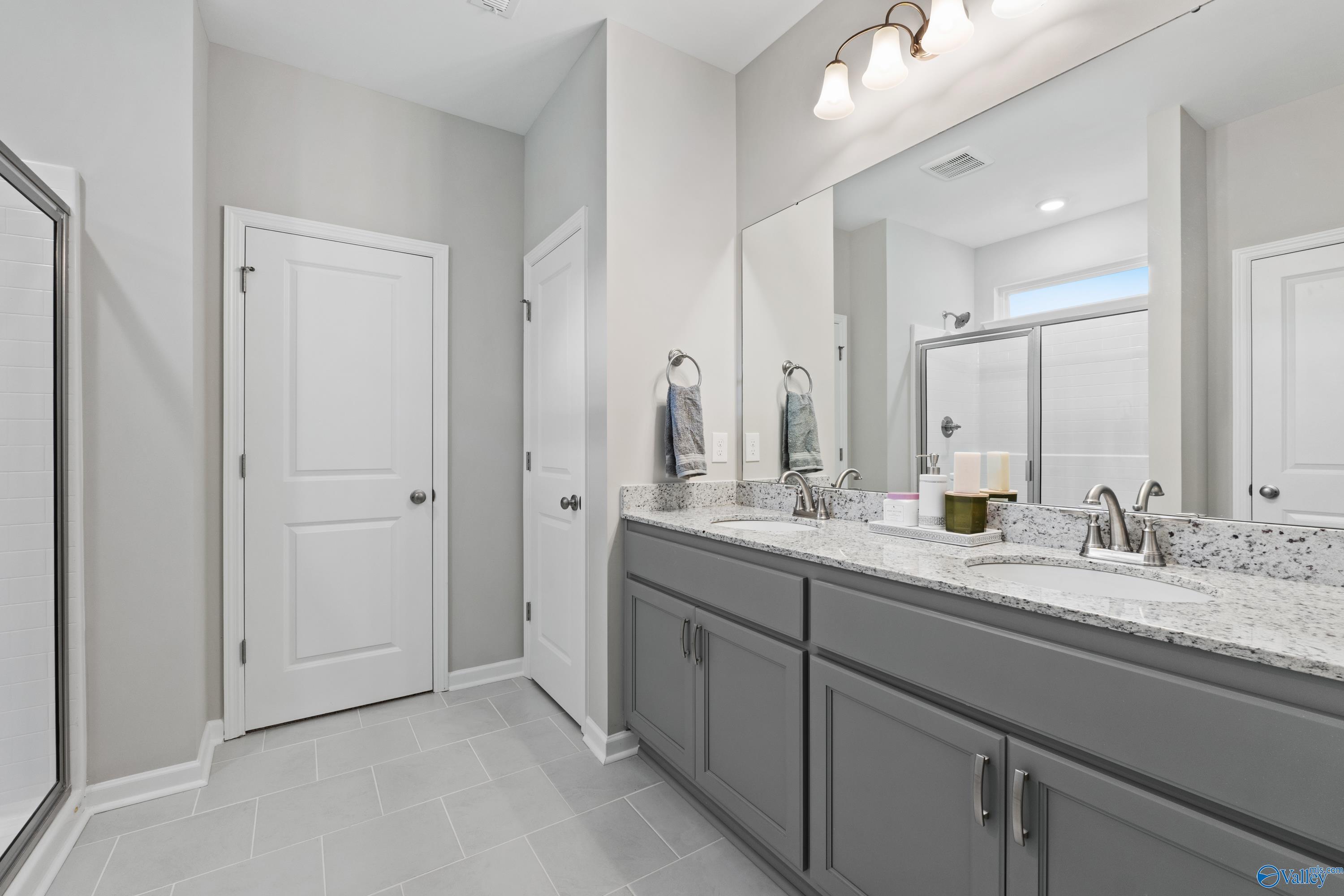 Modern master bathroom with double gray vanity, quartz counters, and glass shower in Davidson Homes The Luna, Hazel Green, Alabama