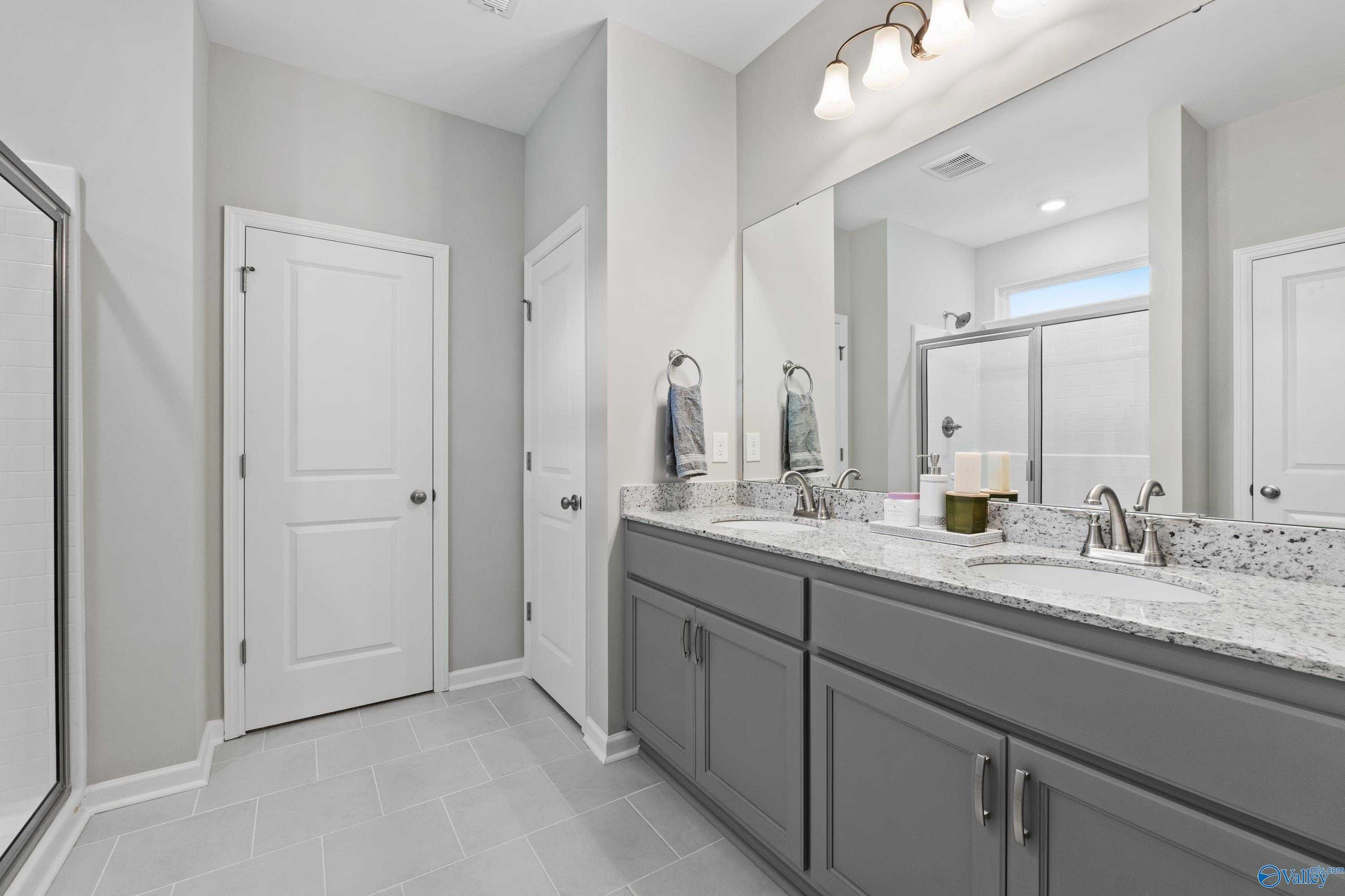 Modern master bathroom with double gray vanity, quartz countertop, large mirror, and glass shower in Davidson Homes The Luna, Hazel Green AL