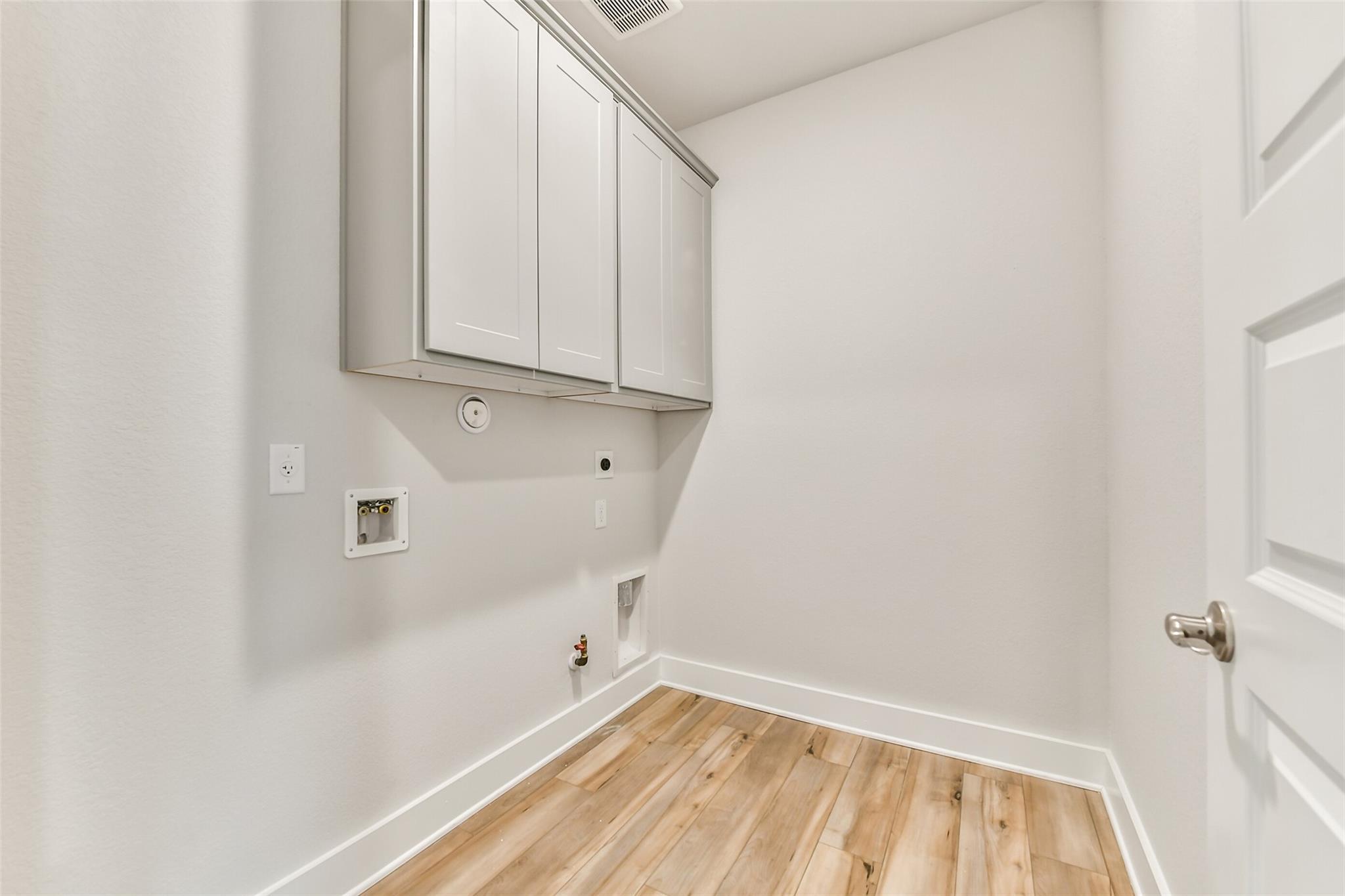 Spacious laundry room with white shaker cabinets, washer hookups and hardwood floors in Davidson Homes The George A, Texas City