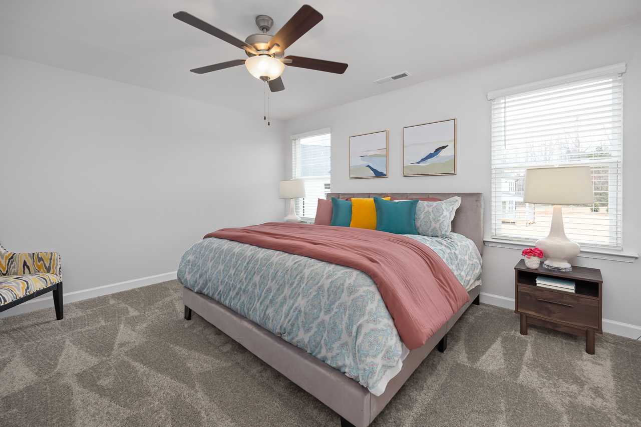 Spacious primary bedroom in Gregory Village Lillington NC by Davidson Homes featuring king bed with colorful bedding and ceiling fan