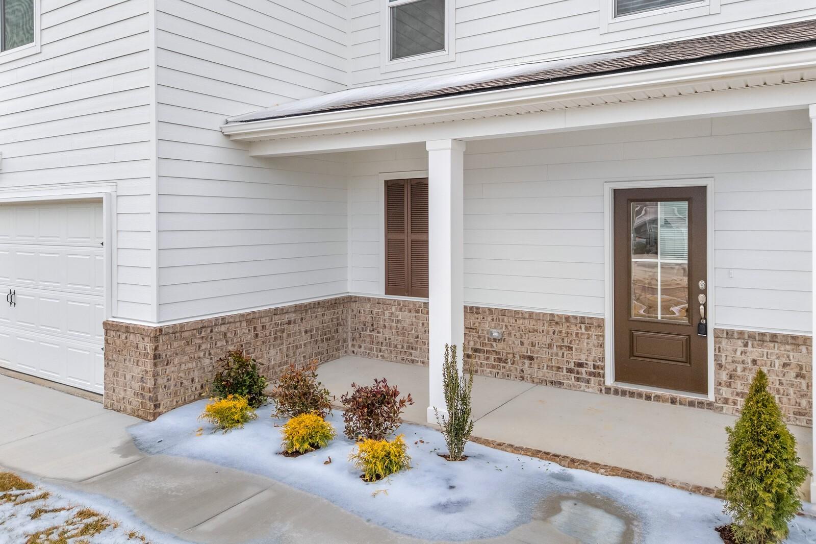 Modern two-story Gordon C home exterior with 2-car garage, covered porch, brick accents, and snowy landscaping in Sage Farms, White House, Tennessee
