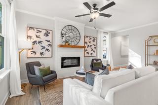 Spacious living room in The Washington H townhome with white sofas, gray armchairs, stone fireplace, abstract bird art, and large windows