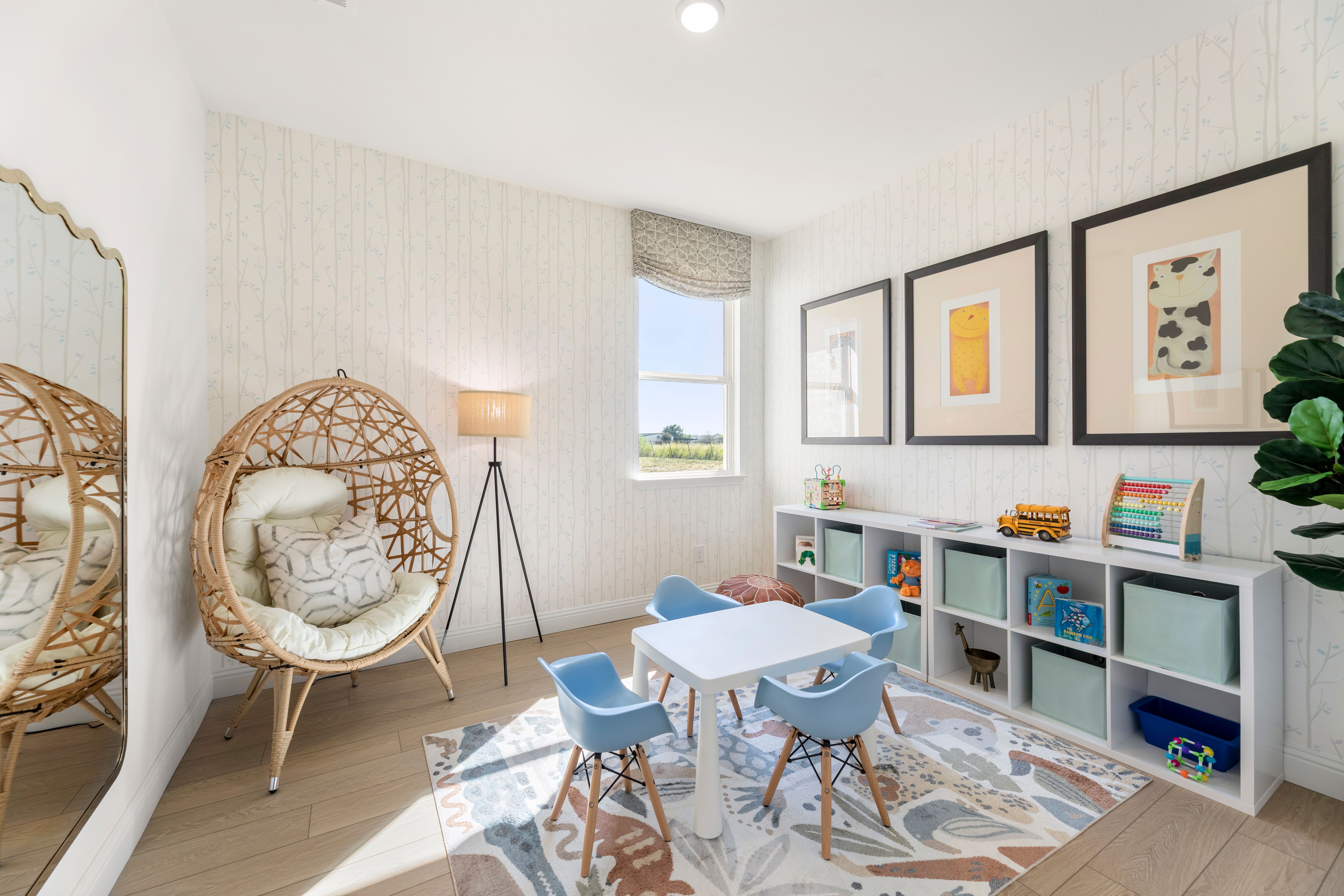 Cozy playroom in The Laurel by Davidson Homes with wicker hanging chairs, blue kids table, toy shelves, and natural light