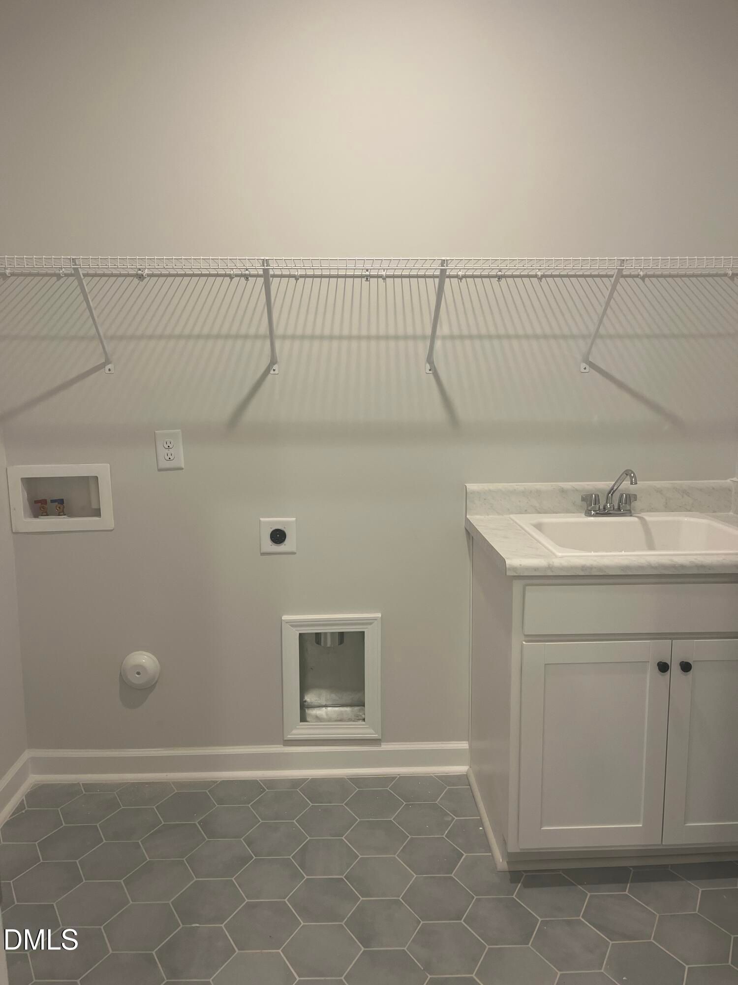 Modern laundry room featuring utility sink, white wire shelving, and gray hexagonal tile in Davidson Homes The Birch II E, Wake Forest, NC