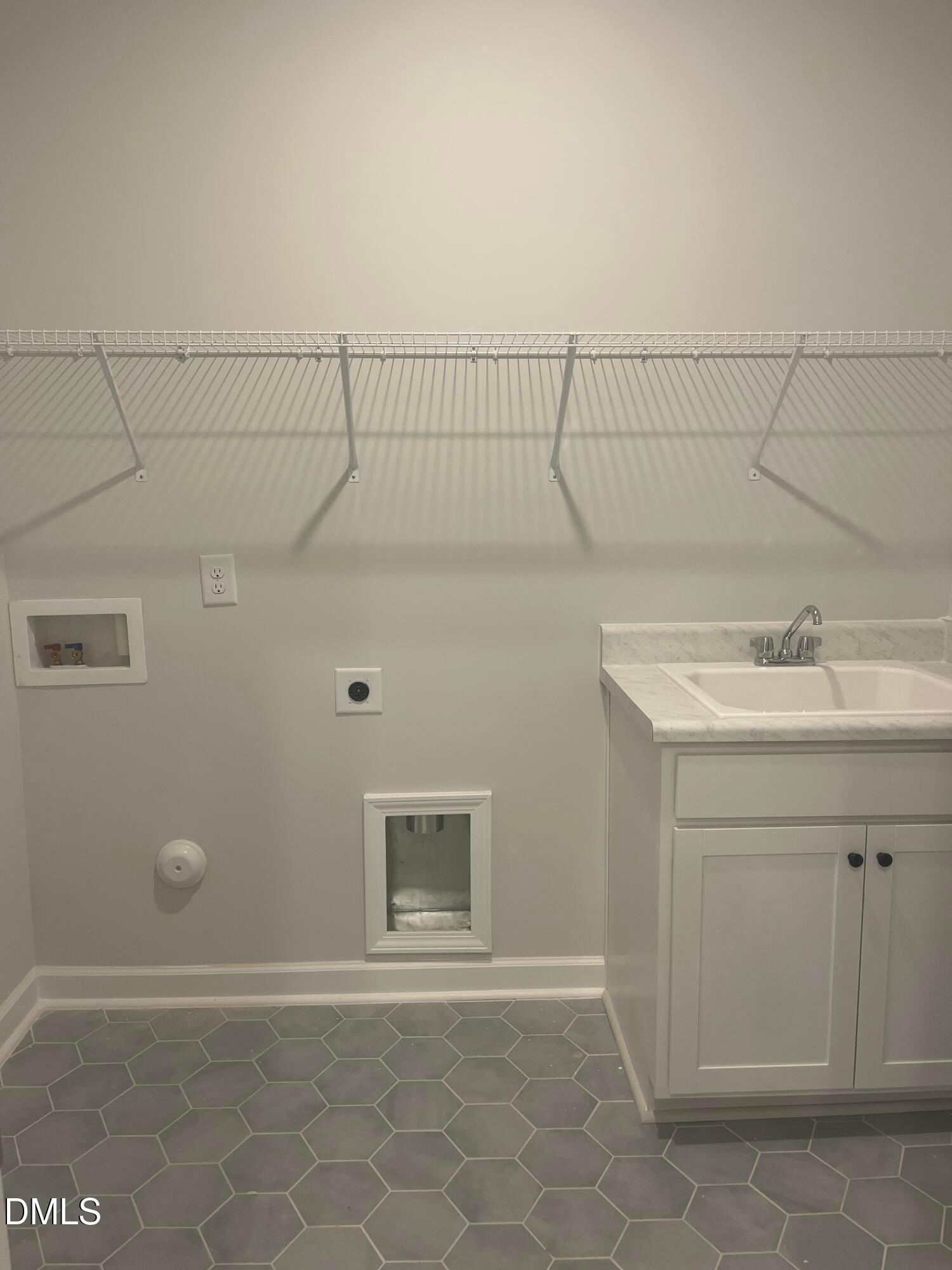 Modern laundry room featuring utility sink, white wire shelving, and gray hexagonal tile in Davidson Homes The Birch II E, Wake Forest, NC