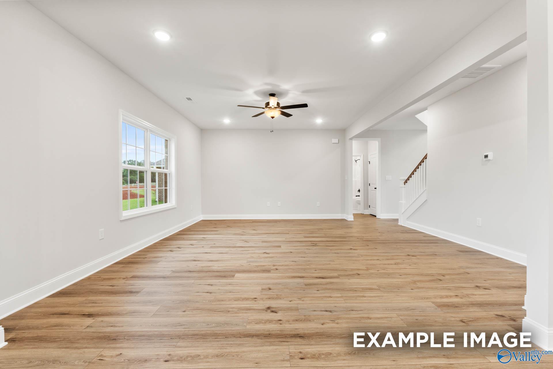 Spacious empty living room with light oak hardwood floors, white walls, ceiling fan, and large window in Davidson Homes Madison B, Toney Alabama