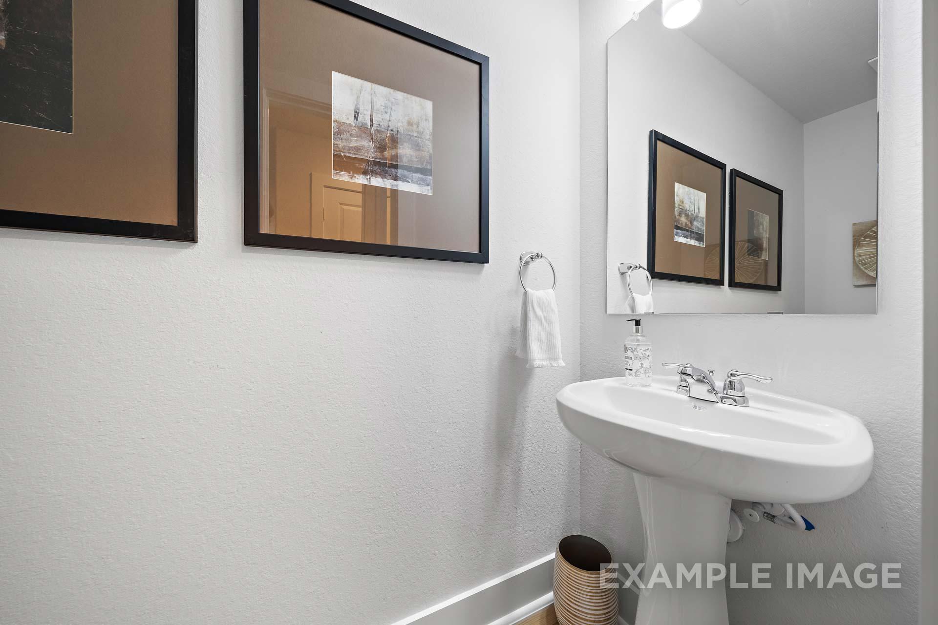 Elegant powder room in The Rose B featuring white pedestal sink, large mirror, and framed wall art