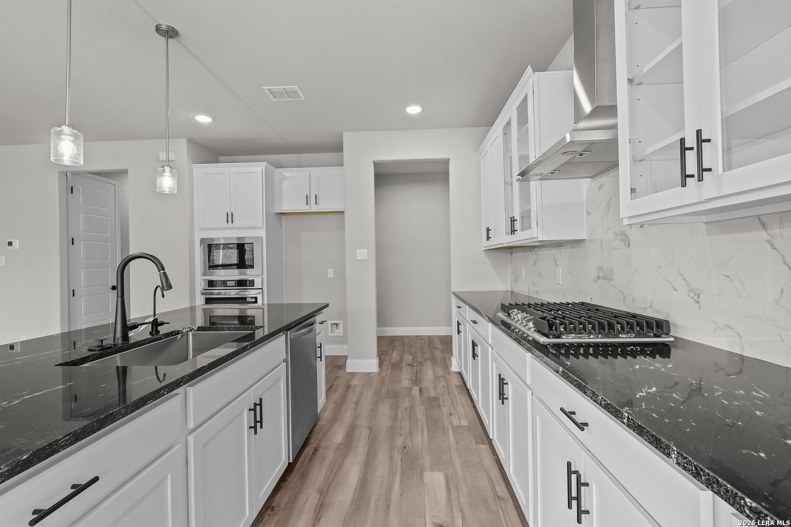 Modern kitchen with white cabinets, black granite island, stainless appliances, gas range in The Belmont H, Castroville TX