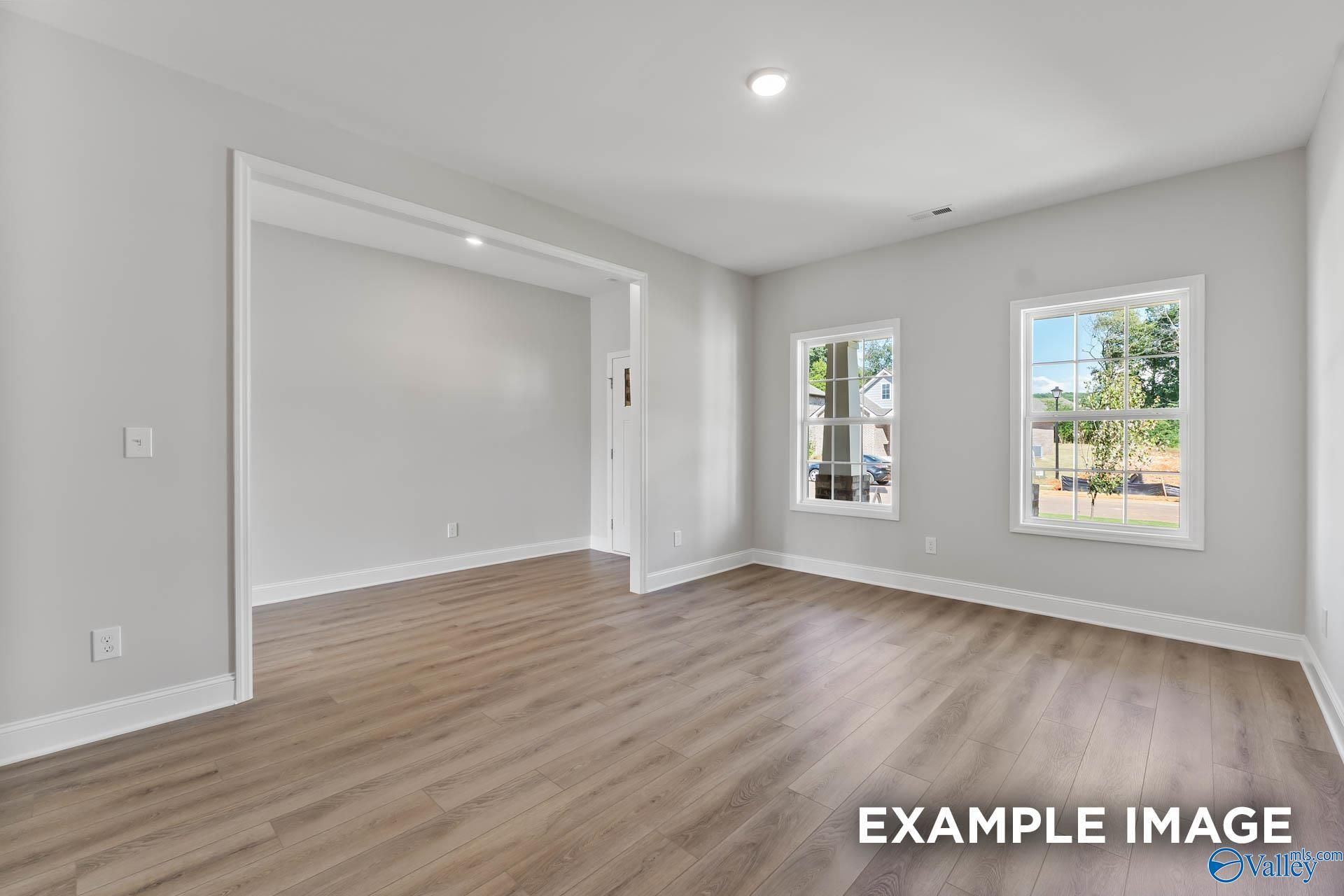 Bright living room with light gray walls, hardwood floors, large windows, and open archway in Davidson Homes The Chelsea D, New Market, AL