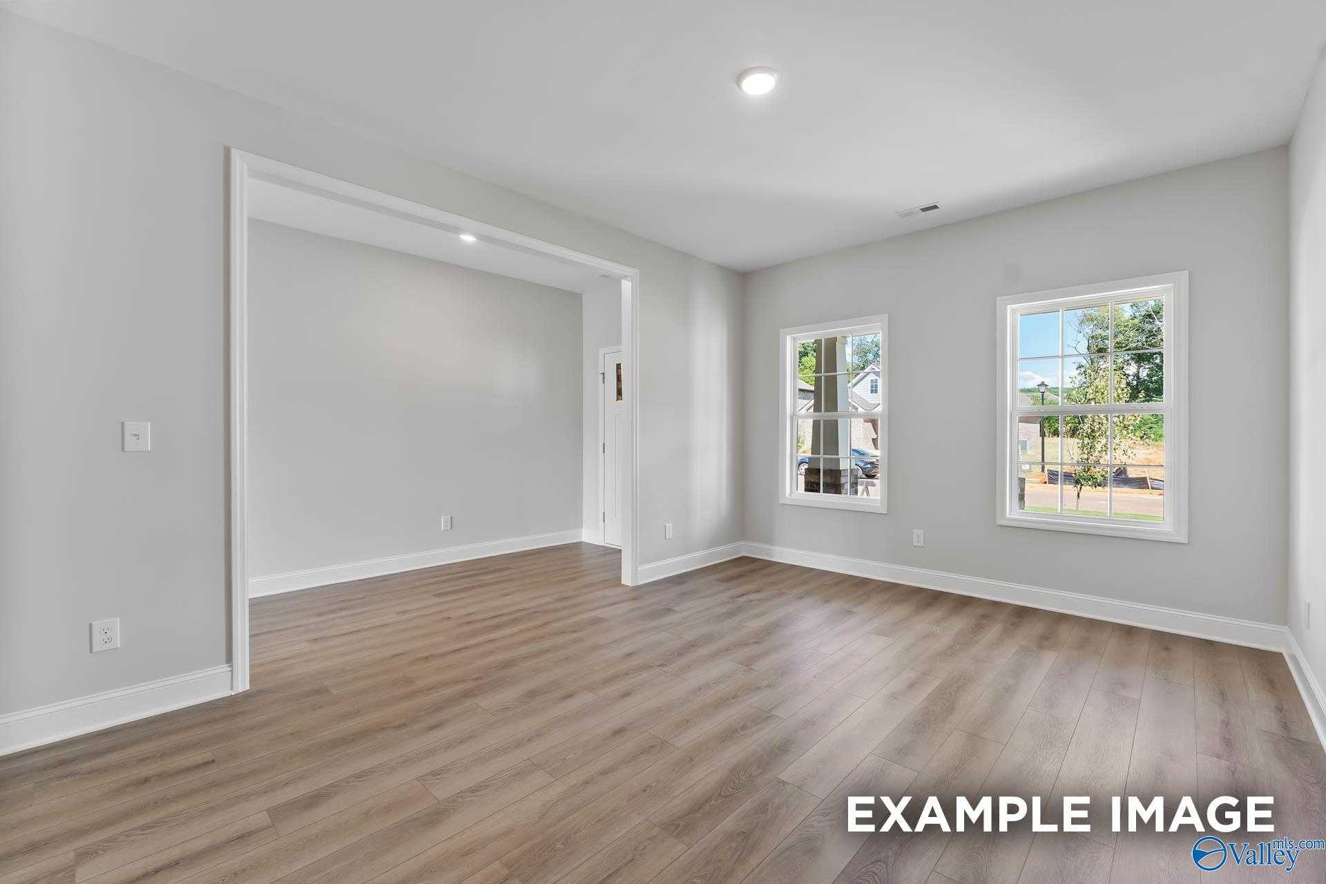 Bright spacious living room with hardwood floors, large windows, and light gray walls in Davidson Homes The Chelsea C, Athens AL