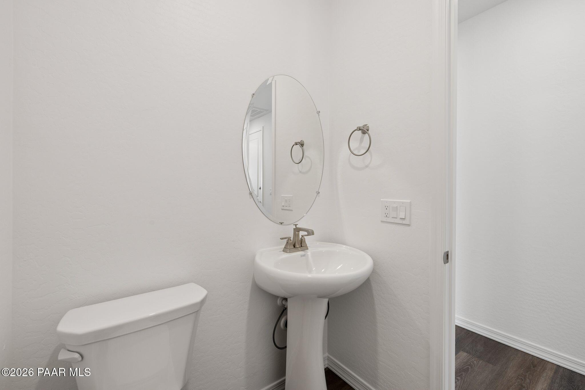 Elegant powder room with white pedestal sink, round mirror, toilet, and hardwood flooring in Davidson Homes The Monarch A, Prescott, AZ