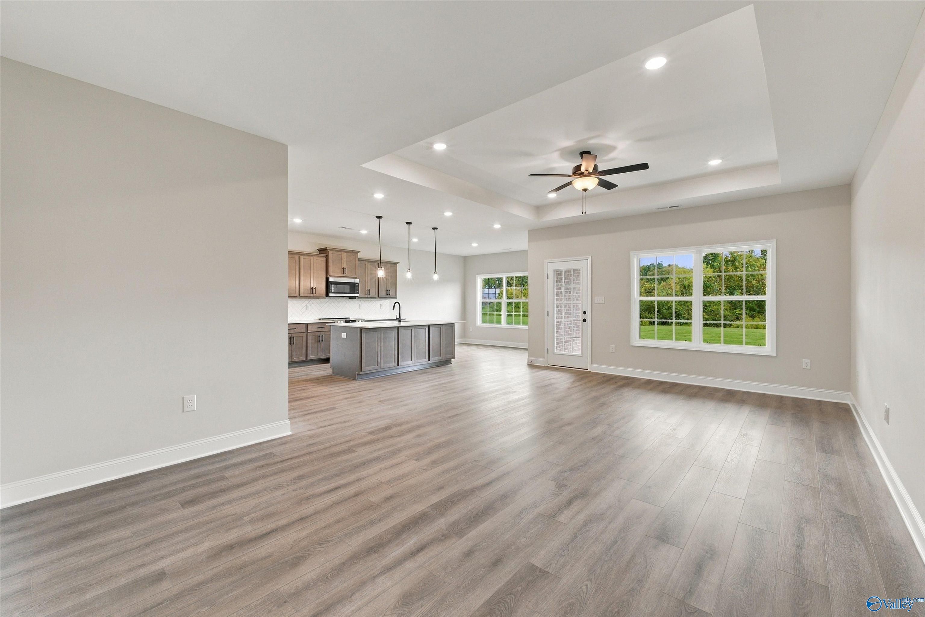 Open-concept living room and kitchen with gray island, wood-look floors, and tray ceiling in The Montgomery, Decatur, Alabama