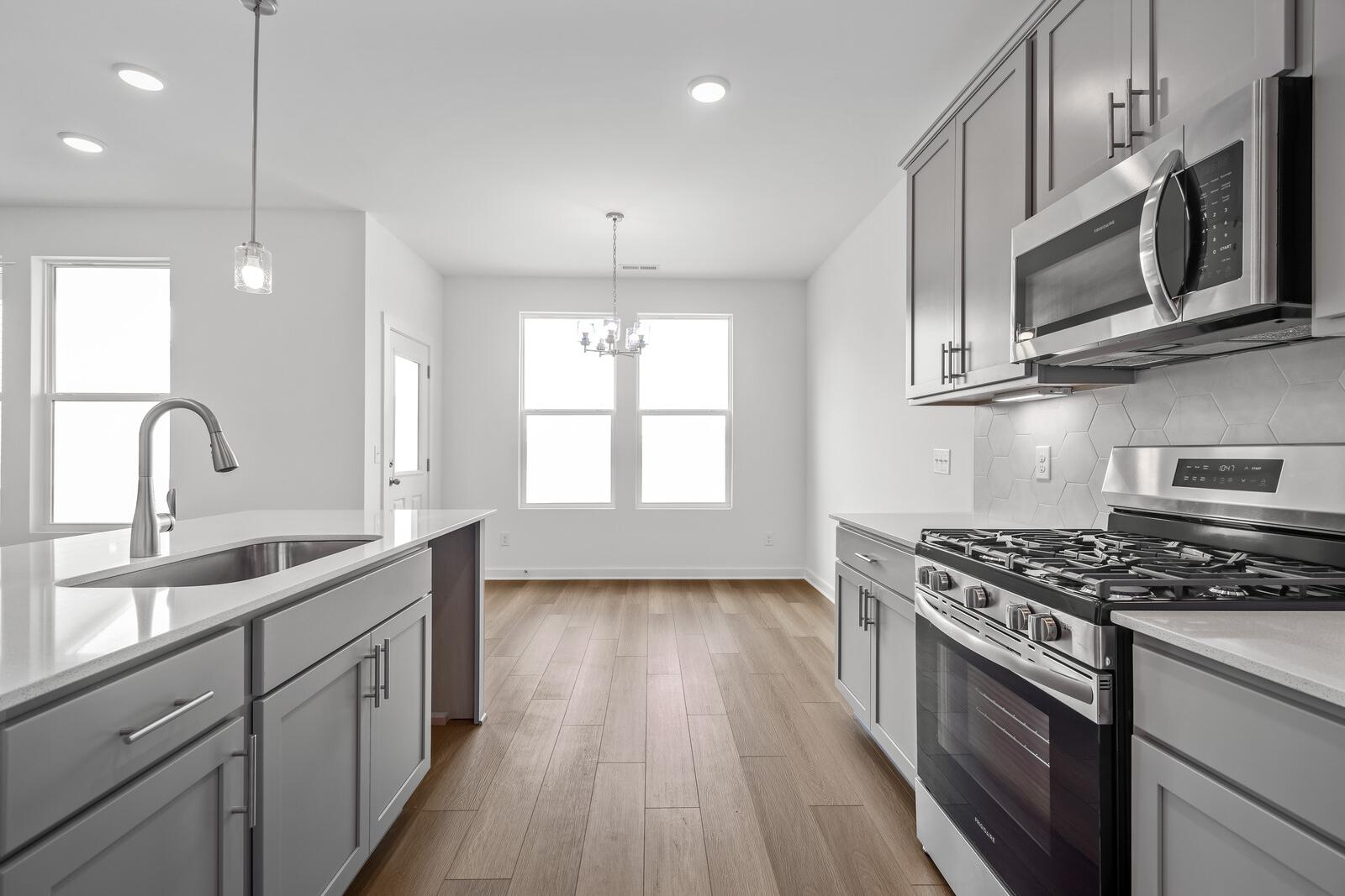 Spacious kitchen in The Asheville home design featuring white quartz island, stainless steel appliances, and open dining area