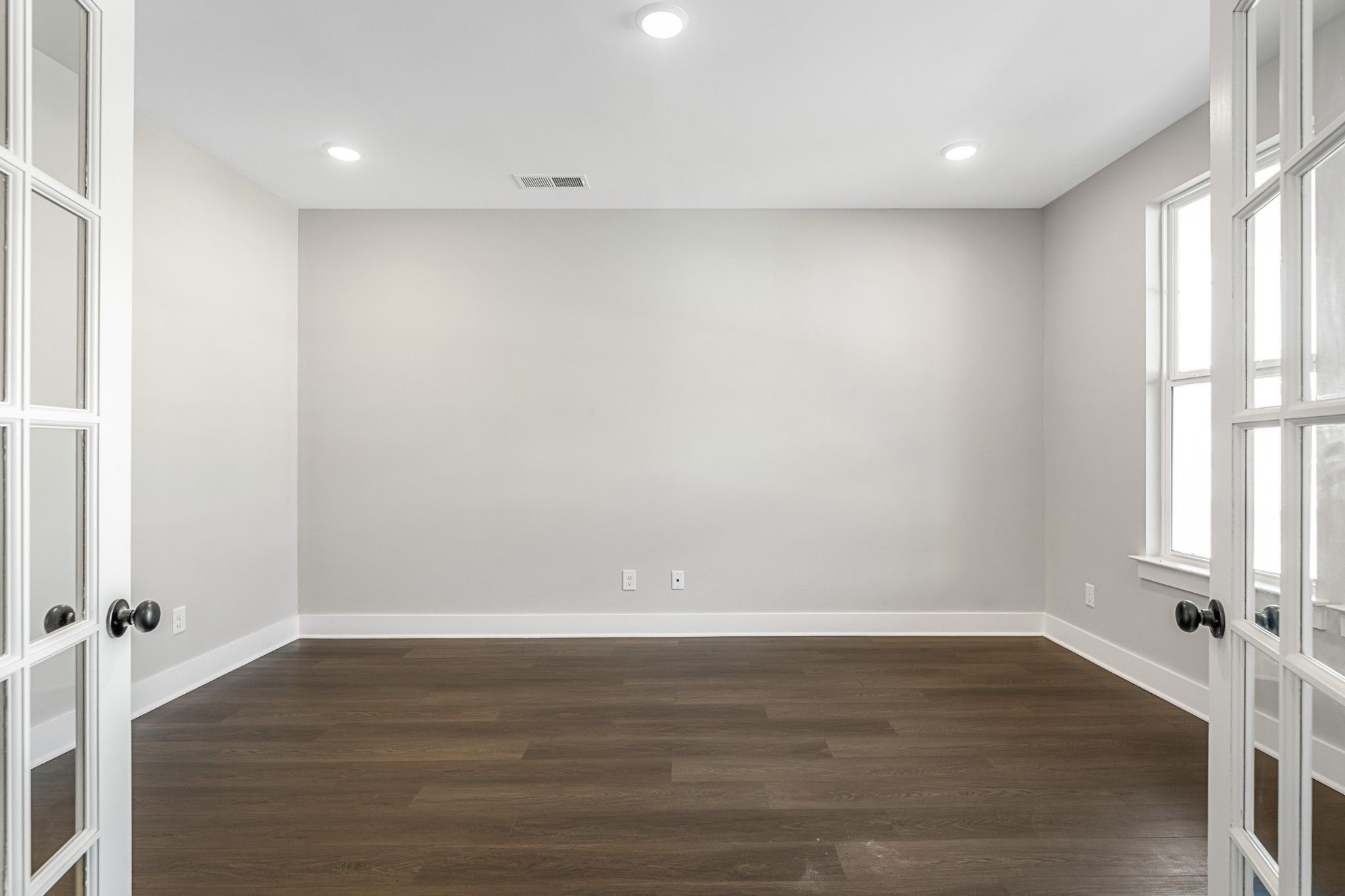 Empty bedroom with open French doors, neutral gray walls, hardwood floors in Davidson Homes The Henry C, White House, TN