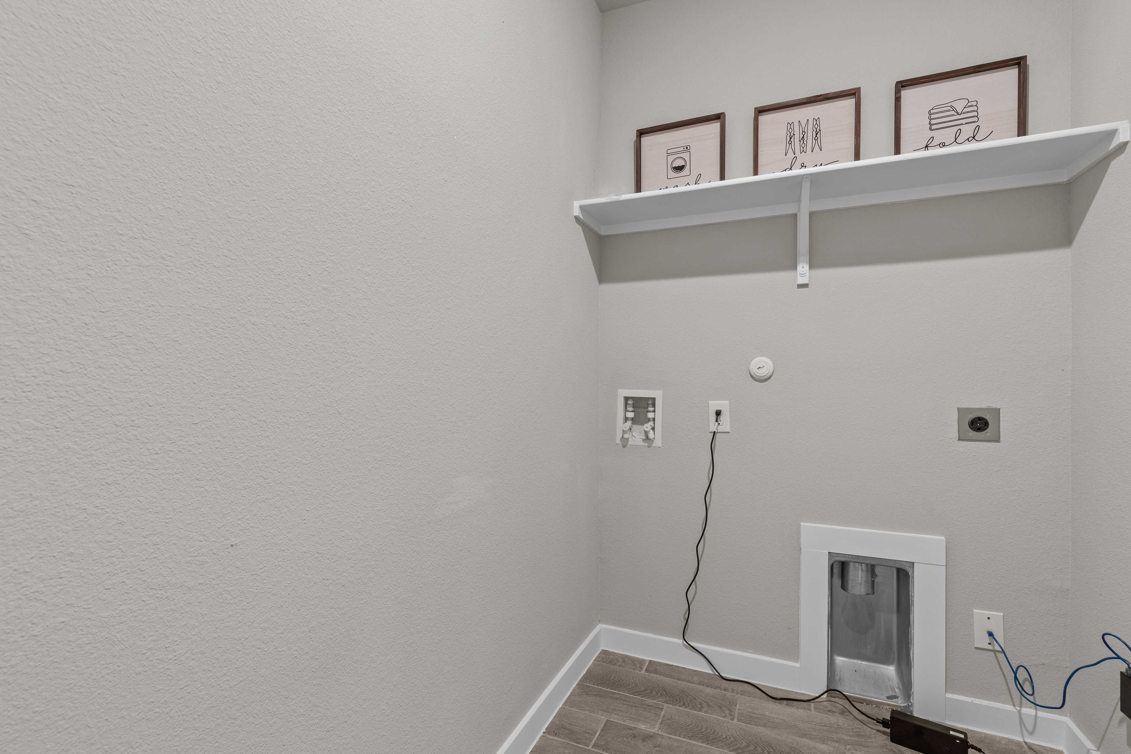 Spacious laundry room at Hannah Heights in Seguin Texas with light gray walls, floating white shelf, art frames, and washer dryer hookups