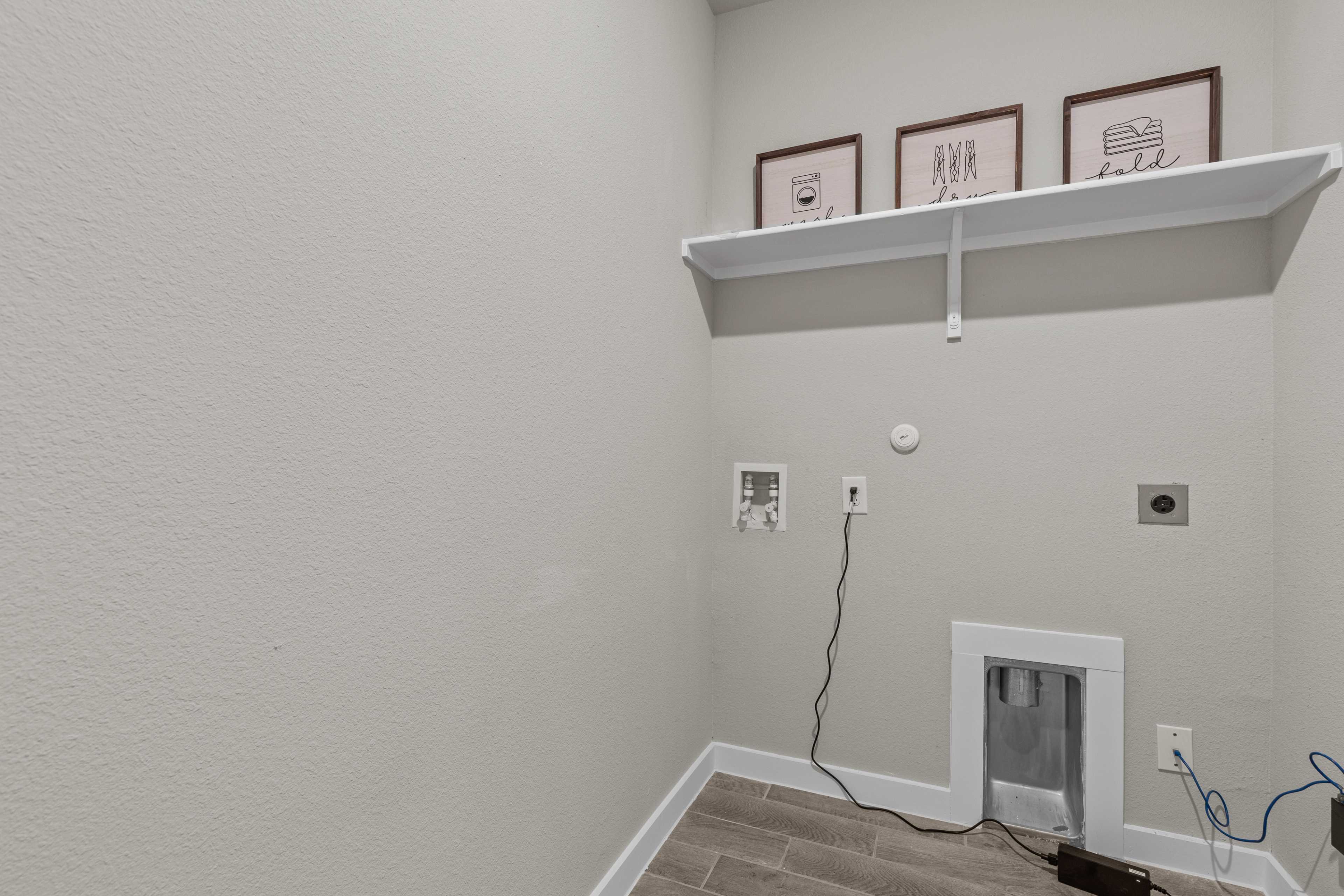 Spacious laundry room at Hannah Heights in Seguin Texas with light gray walls, floating white shelf, art frames, and washer dryer hookups