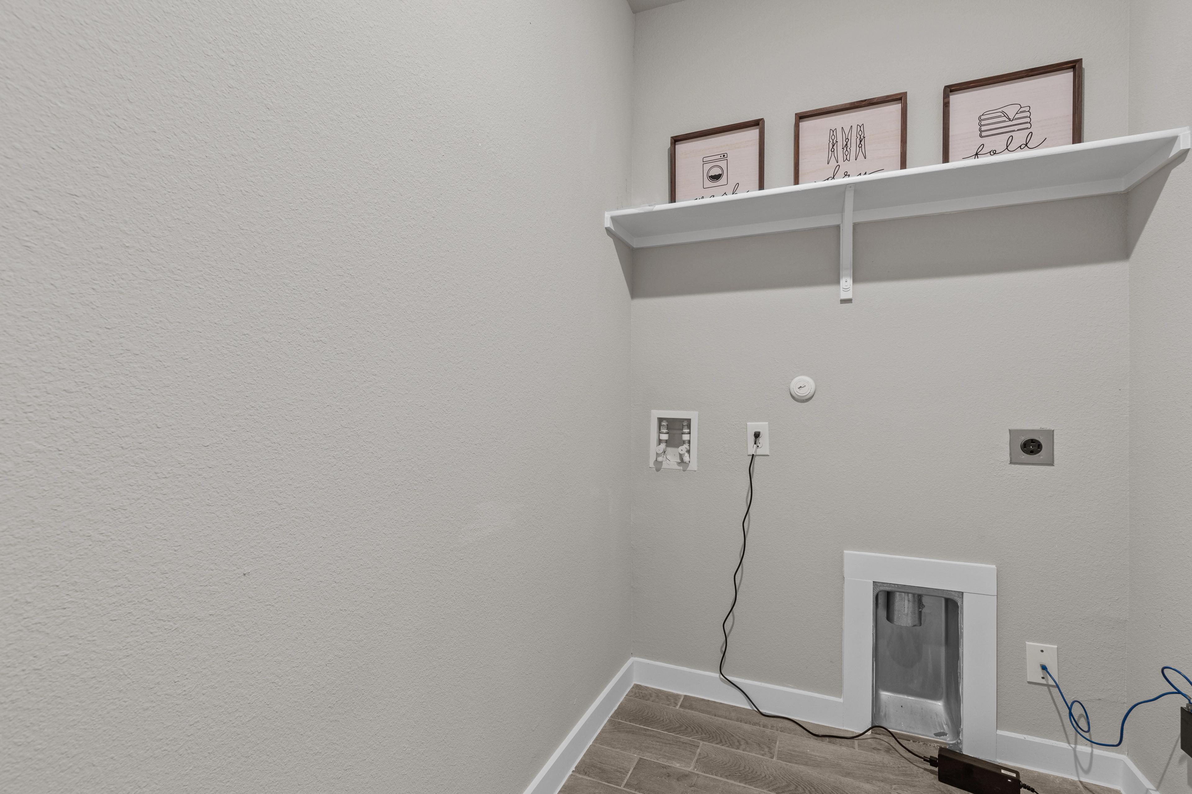 Spacious laundry room at Hannah Heights in Seguin Texas with light gray walls, floating white shelf, art frames, and washer dryer hookups